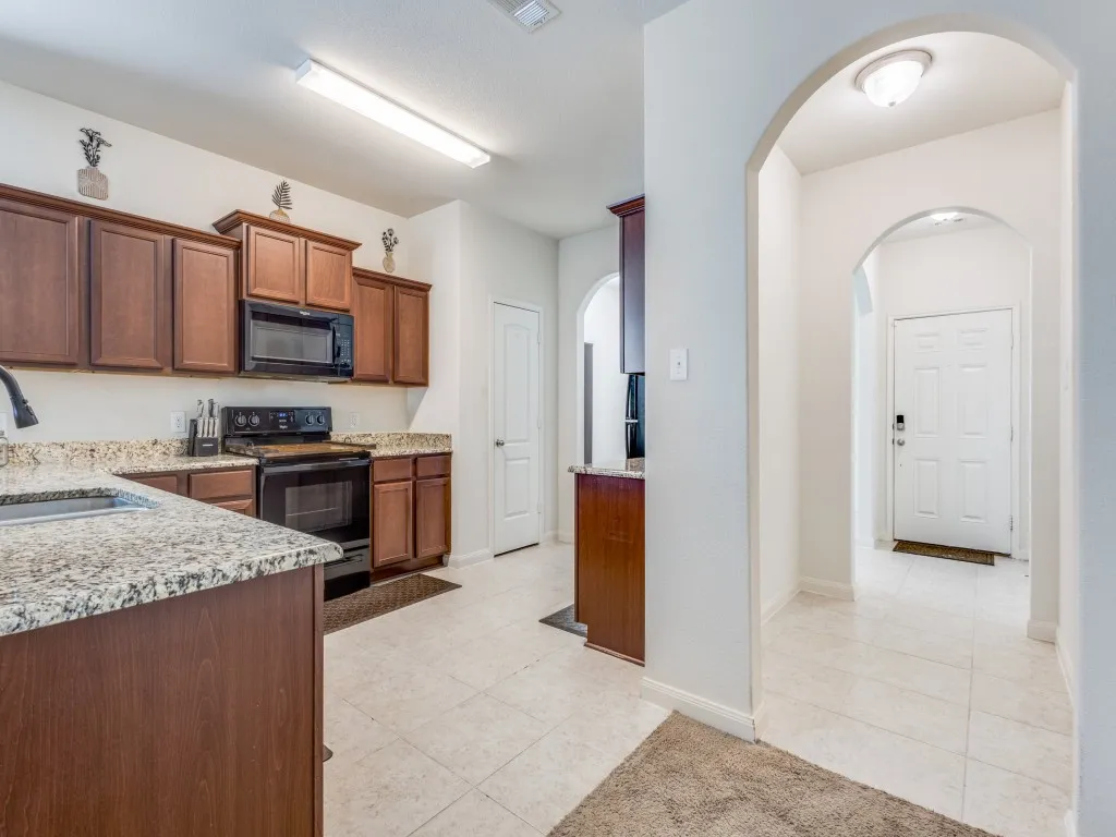 Kitchen featuring black appliances, light stone counters, arched walkways, and light tile patterned flooring