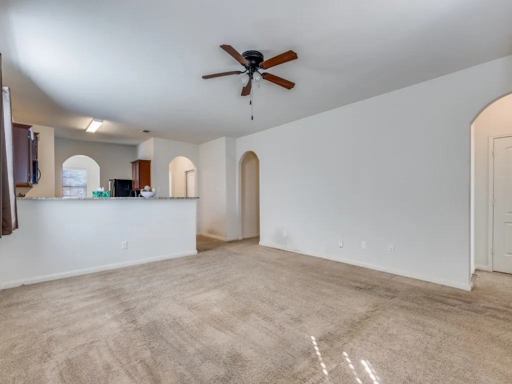 Unfurnished living room featuring arched walkways, light colored carpet, and a ceiling fan