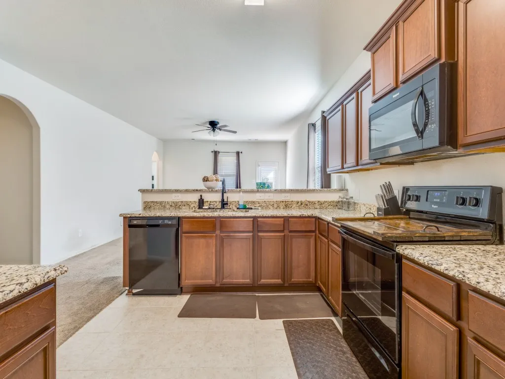 Kitchen featuring black appliances, wood finish cabinets, a peninsula, light stone counters, and arched walkways