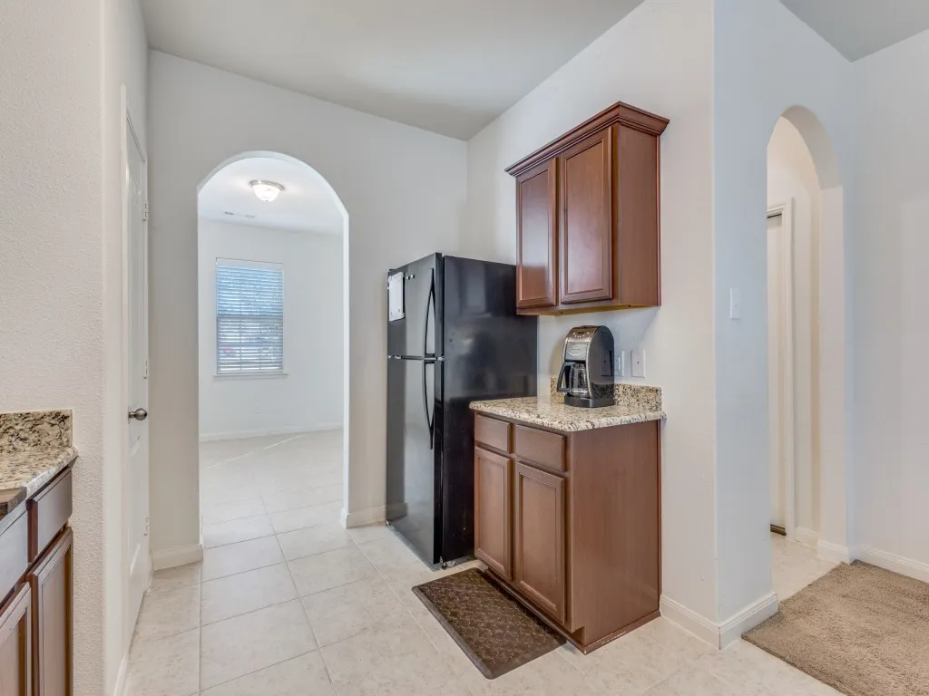 Kitchen with arched walkways, freestanding refrigerator, light stone counters, light tile patterned floors, and wood finish cabinets