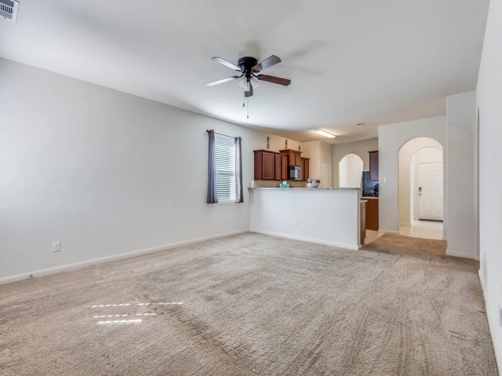 Unfurnished living room with arched walkways, a ceiling fan, and light colored carpet
