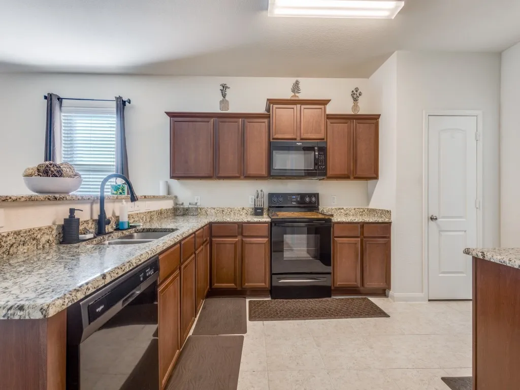 Kitchen featuring black appliances, light stone countertops, wood finish cabinets, and a peninsula