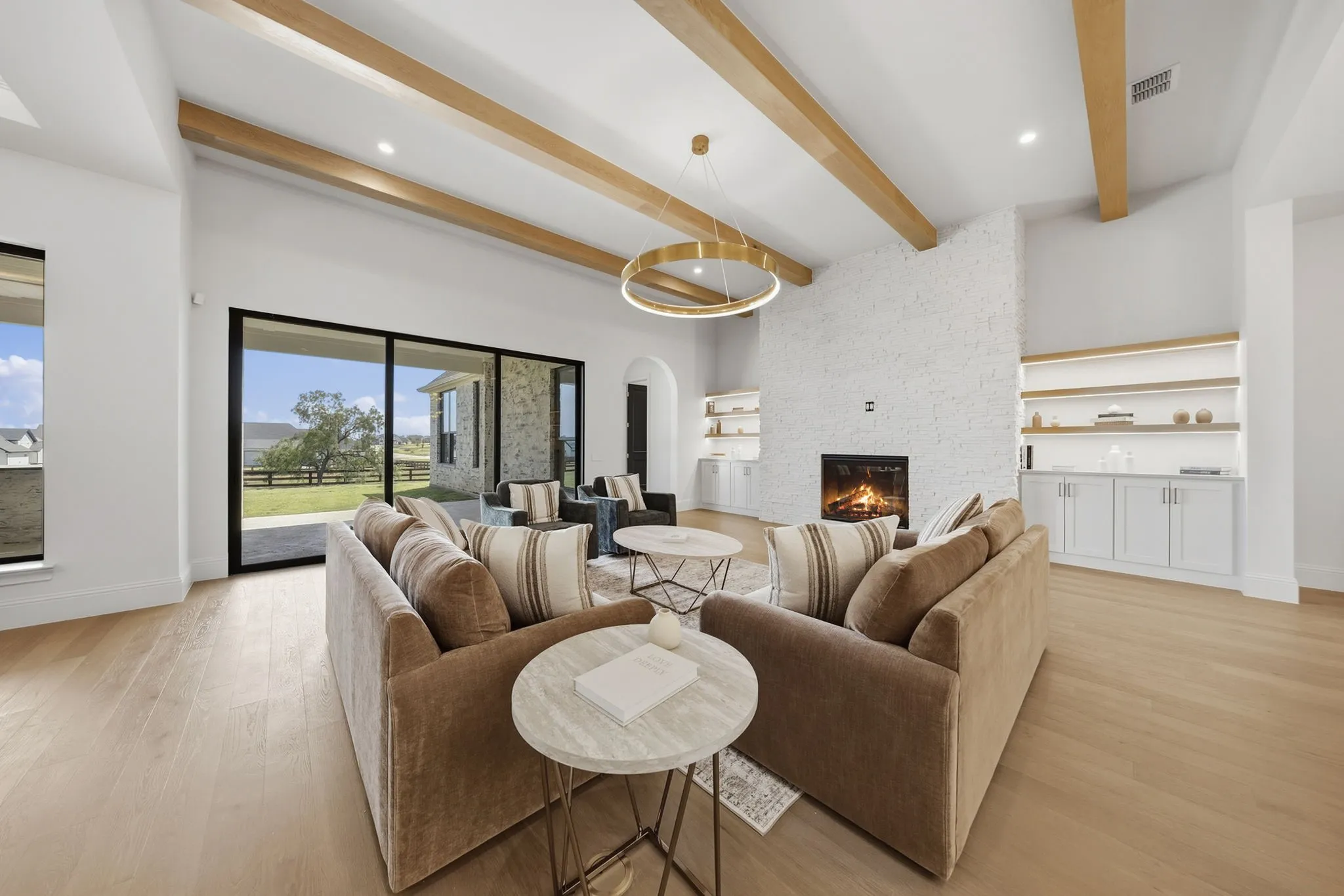Vaulted ceiling with exposed wood beams, expansive sliding glass doors, white brick fireplace, built-in shelving, and wood-finish flooring