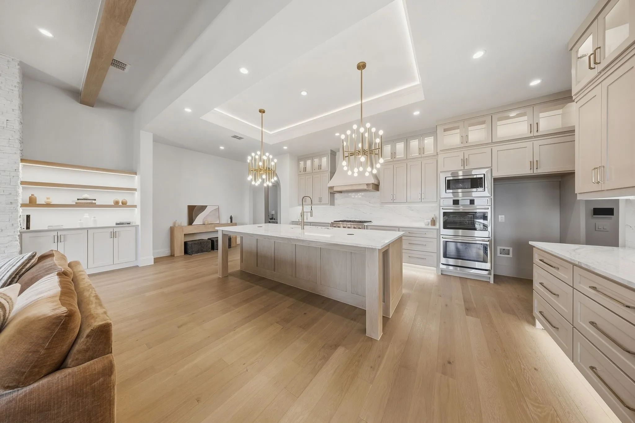 Expansive kitchen featuring a large central island with countertop, extensive cabinetry, built-in double ovens, and wood-finish flooring