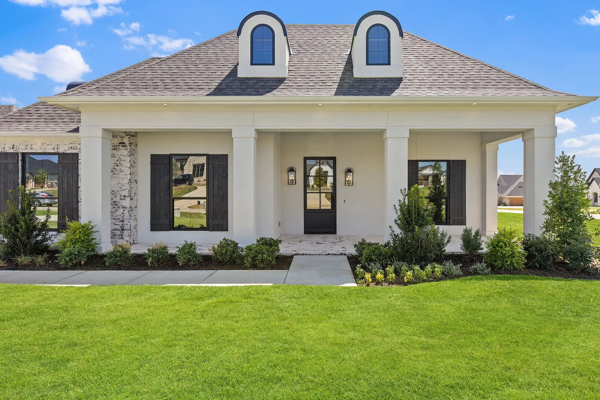 French Colonial exterior featuring a covered porch with square columns, white-painted brick accents, and a dark-framed glass paneled entry door