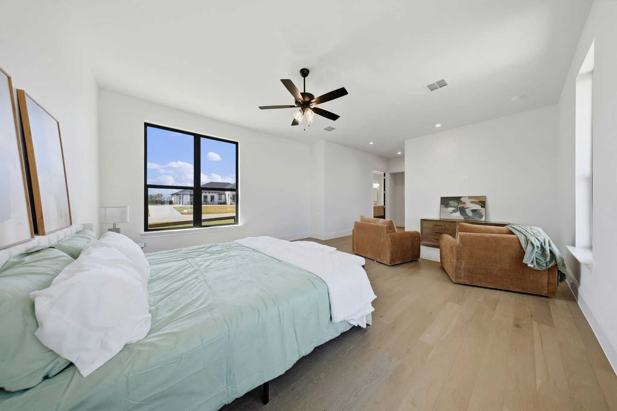 Light wood-finish flooring, a contemporary ceiling fan, and recessed lighting illuminate the spacious room