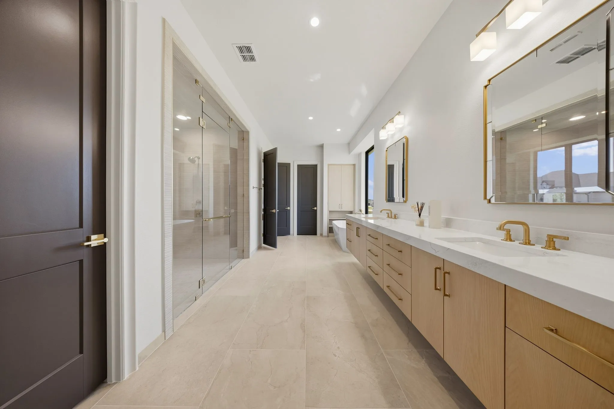 Dual vanity with undermount sinks, light wood-finish cabinetry, gold-tone hardware and fixtures, and a glass-enclosed shower