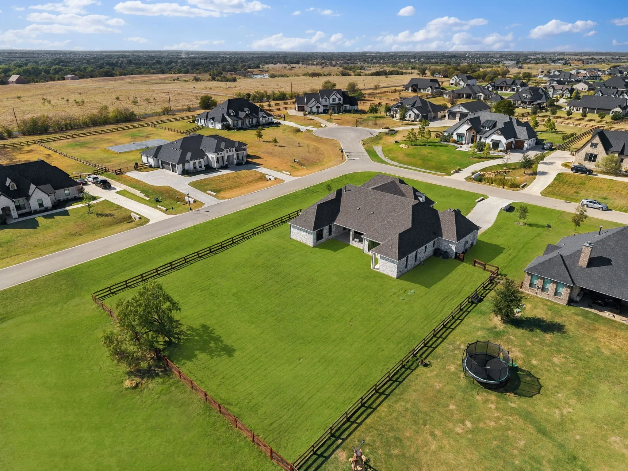 Expansive grassy yard with perimeter fencing, mature tree, and a stone exterior residence featuring a multi-gabled roof
