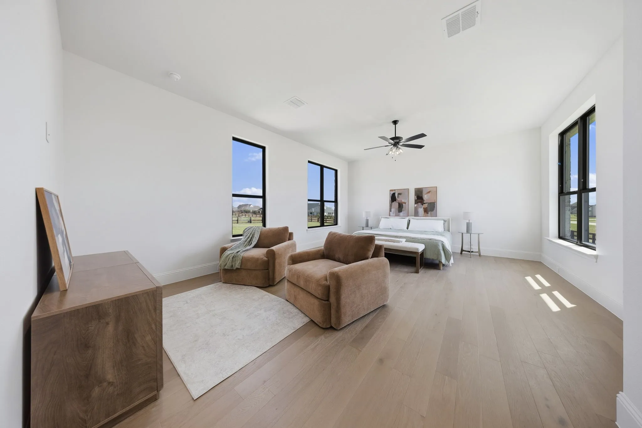 Spacious room with light wood-finish flooring, multiple large windows with dark frames, and a ceiling fan with integrated lighting