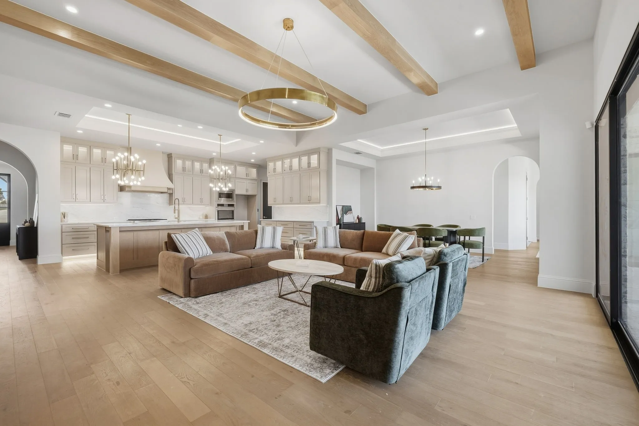 Open-concept living space featuring wood-finish flooring, exposed ceiling beams, recessed lighting, and expansive glass sliding doors
