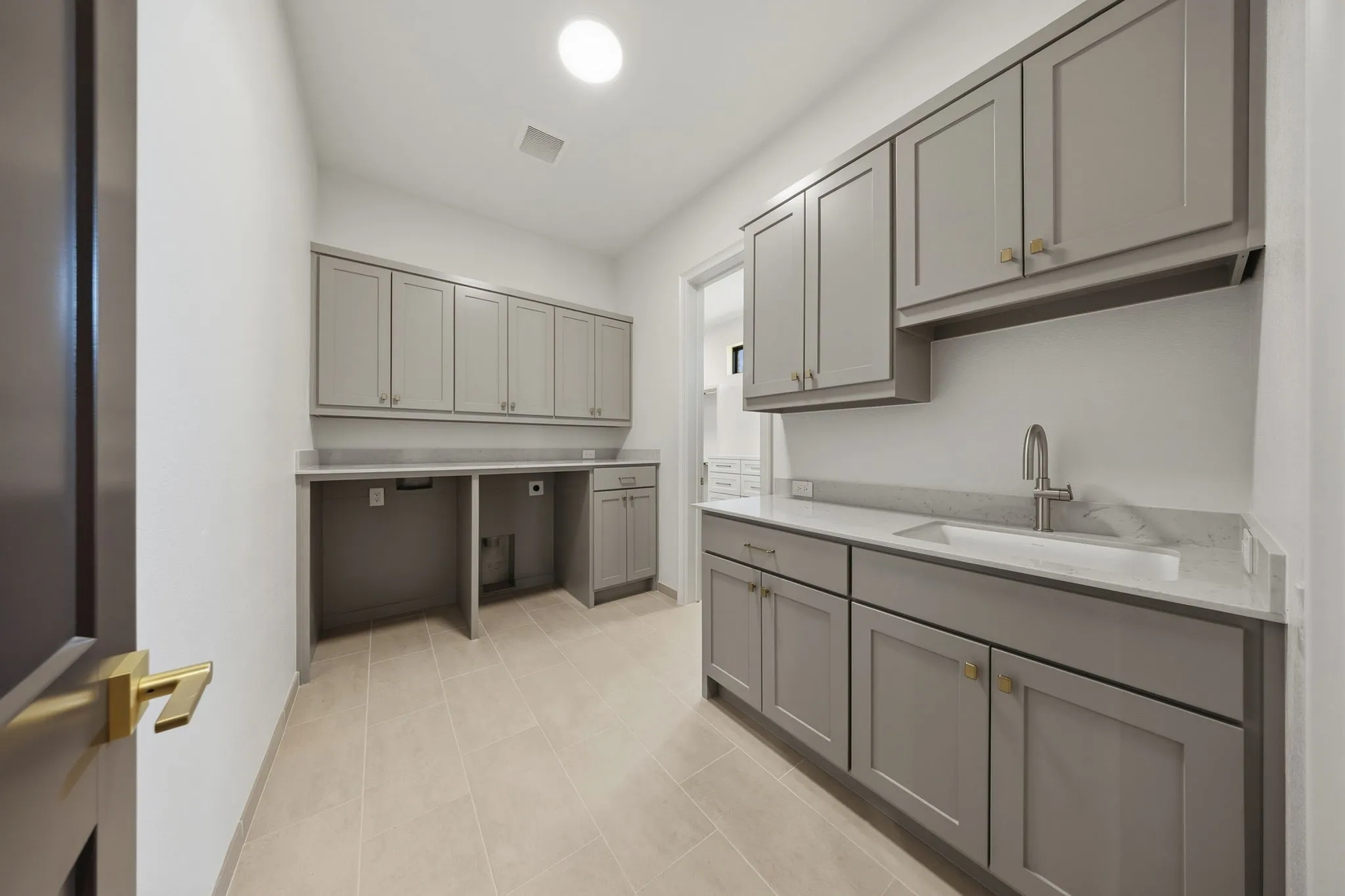 Utility room featuring light gray cabinetry, light-toned tile flooring, recessed sink, and brushed nickel fixtures