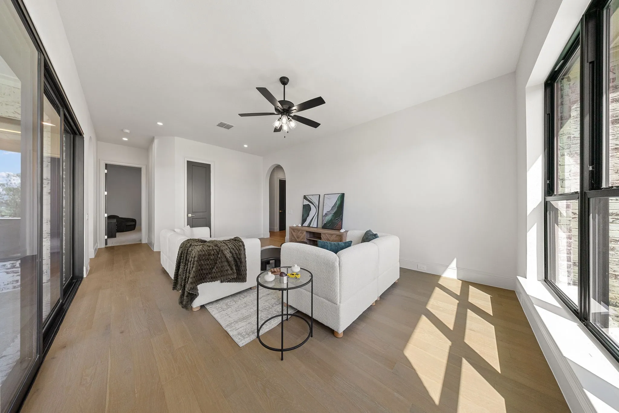 Spacious living area featuring wood-finish flooring, a ceiling fan, large sliding glass doors, and tall windows