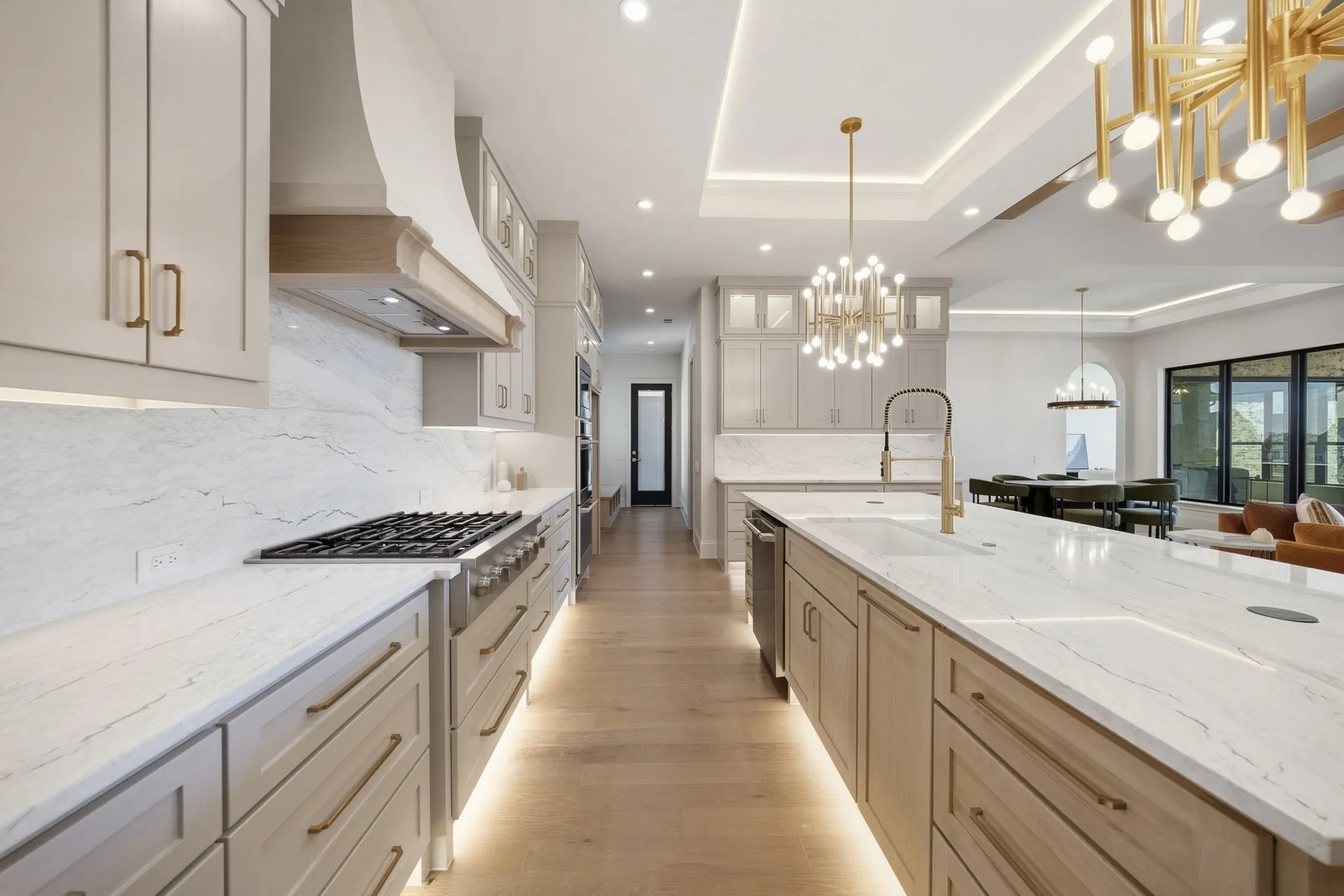 Expansive kitchen featuring a gas range, white stone countertops, wood-finish flooring, recessed lighting, and a large central island with a sink