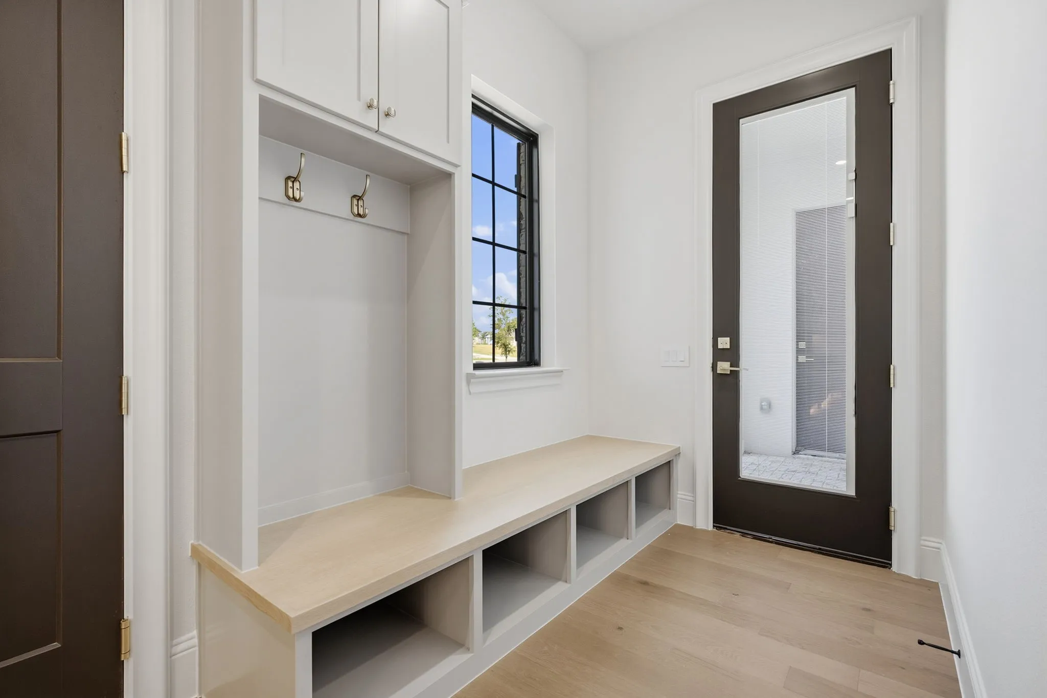 Built-in mudroom bench with cubby storage, upper cabinetry, and coat hooks