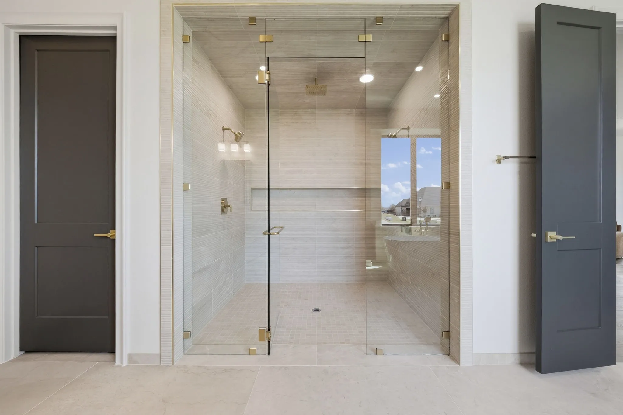 Walk-in glass shower enclosure with brass hardware, tiled walls, and built-in shelving