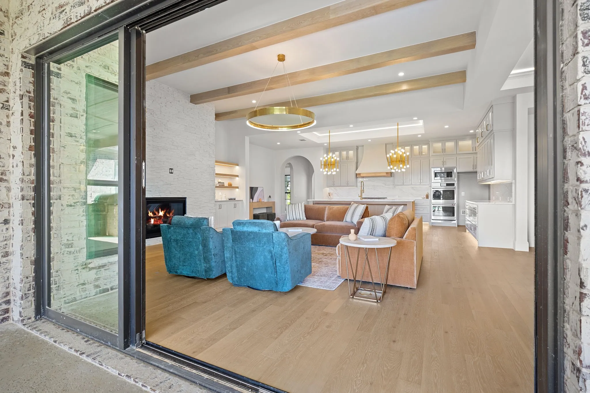 Sliding glass doors opening to a living area featuring wood-finish flooring, exposed ceiling beams, a built-in fireplace, and a kitchen with integrated appliances