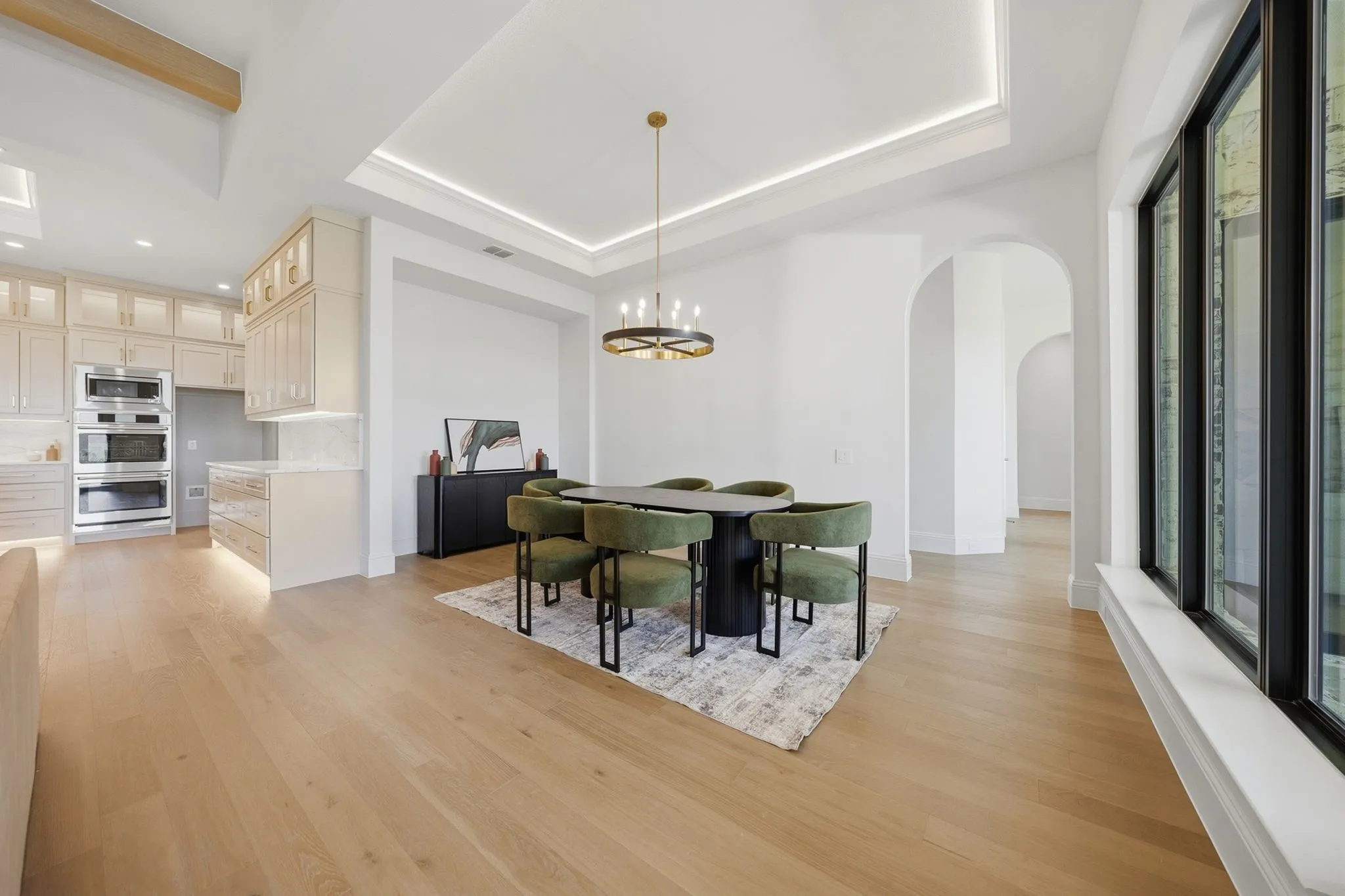 Spacious open concept living area featuring light wood-finish flooring, a coffered ceiling with recessed lighting, and large black-framed windows