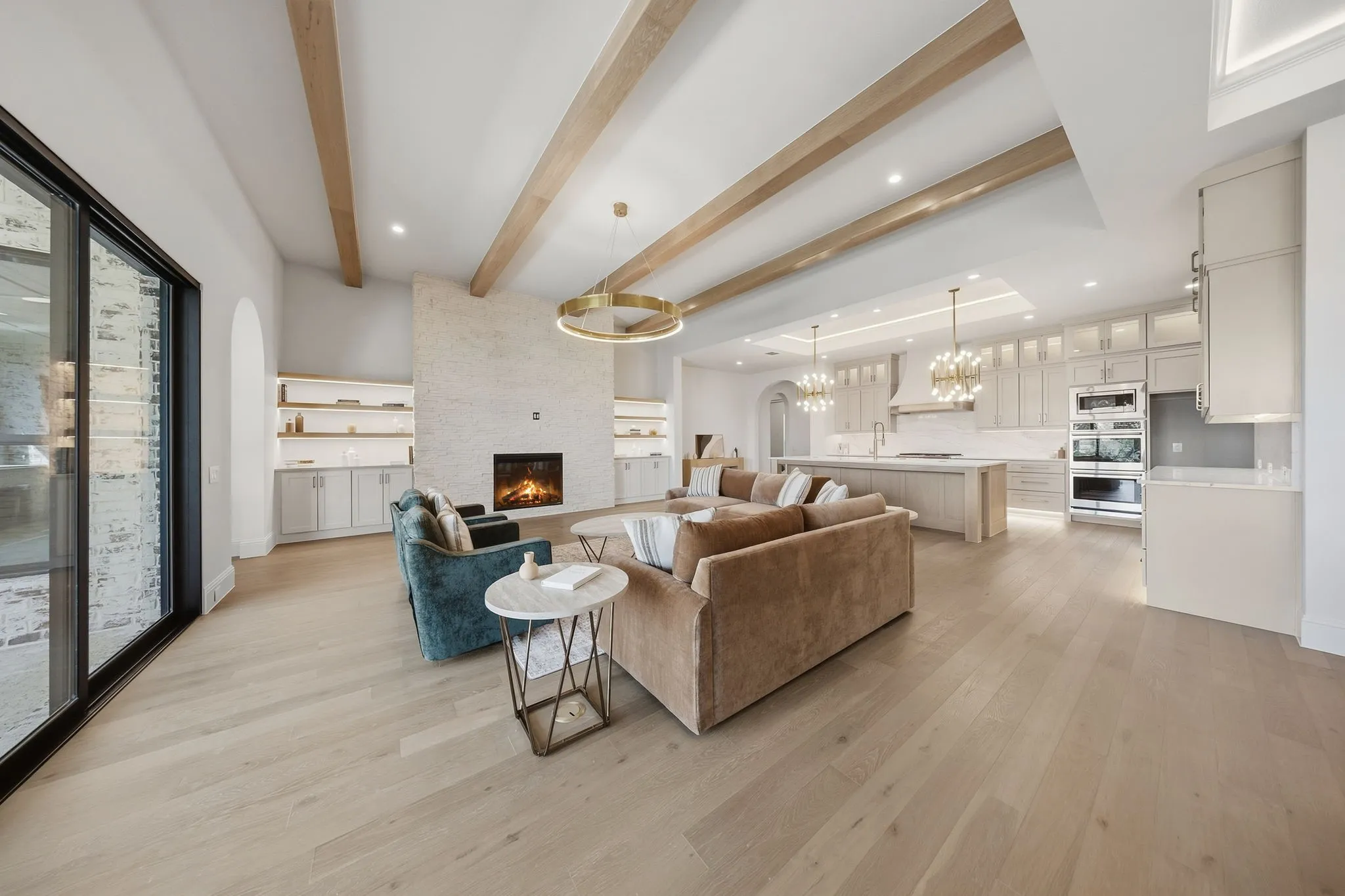 Expansive living space featuring wood-finish flooring, a stone-clad fireplace, and exposed ceiling beams