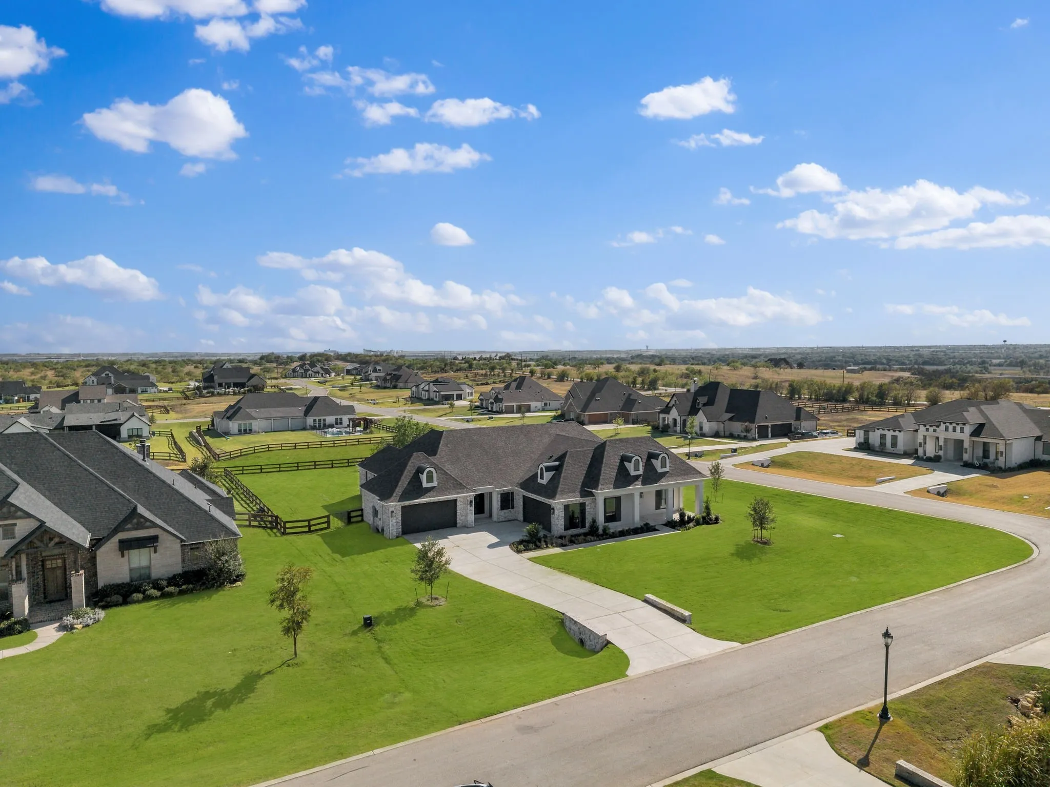 Expansive property featuring a paved driveway, manicured lawn, and a black fenced backyard