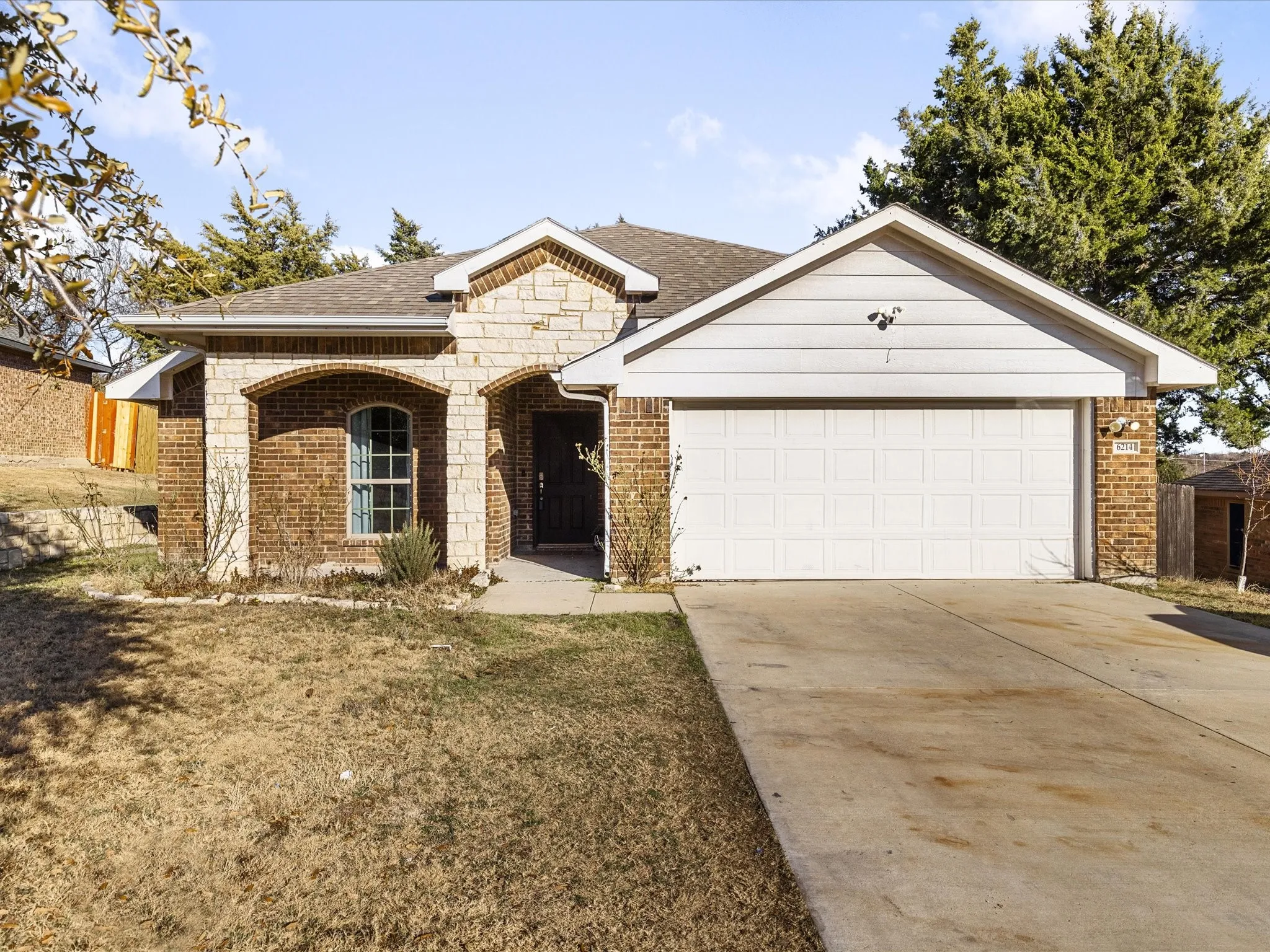 View of front facade featuring a shingled roof, covered porch, brick siding, concrete driveway, and a front lawn