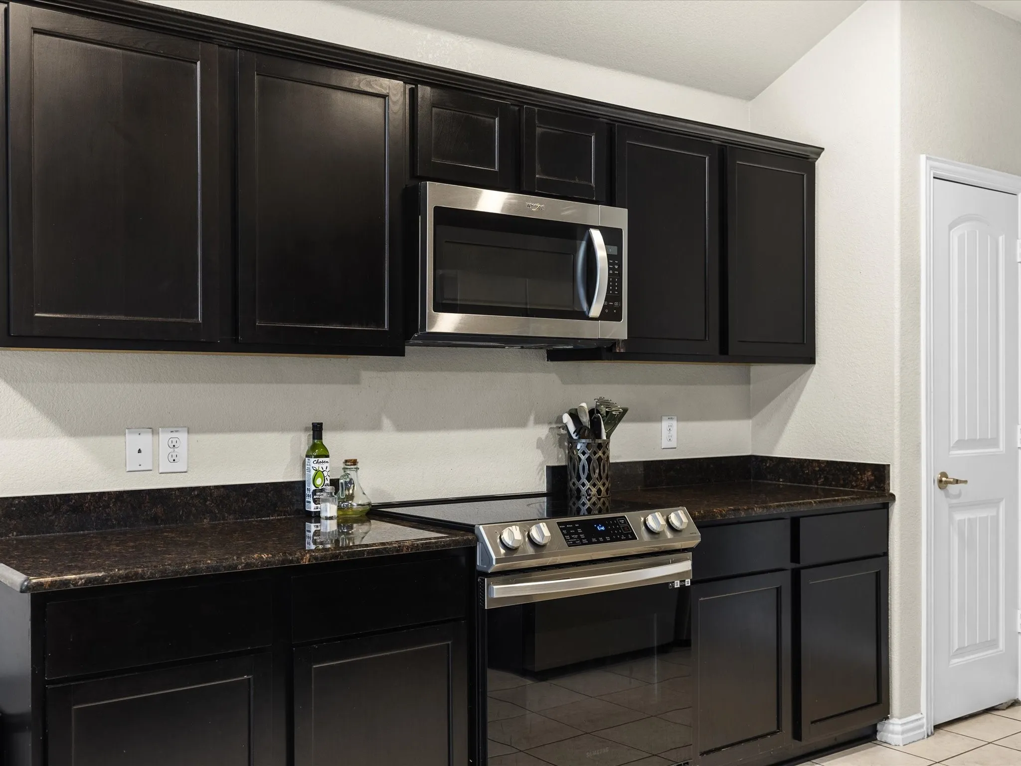 Kitchen with dark cabinets, stainless steel appliances, light tile patterned floors, and dark stone counters