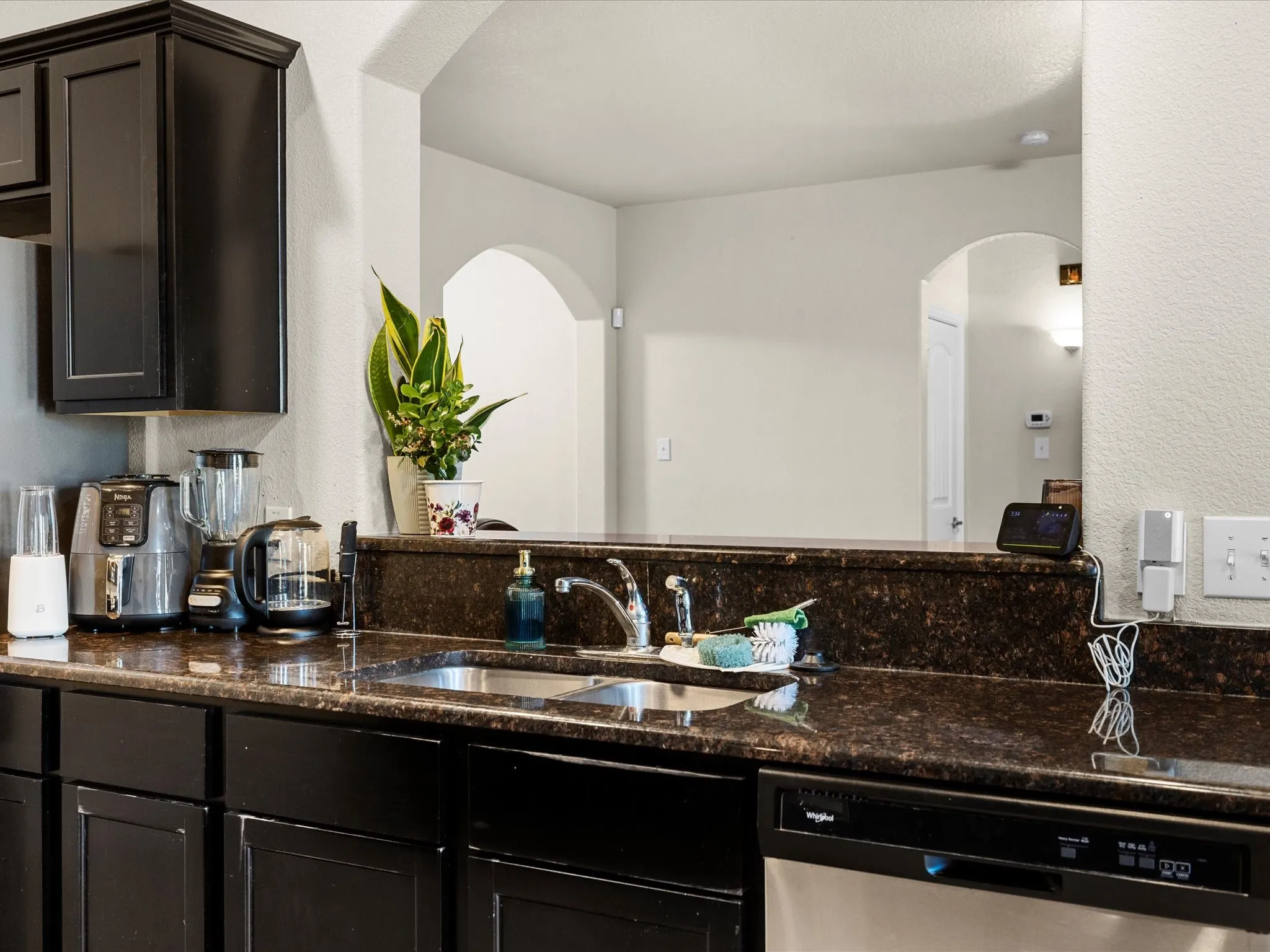 Kitchen featuring dishwasher, dark stone countertops, a textured wall, and arched walkways