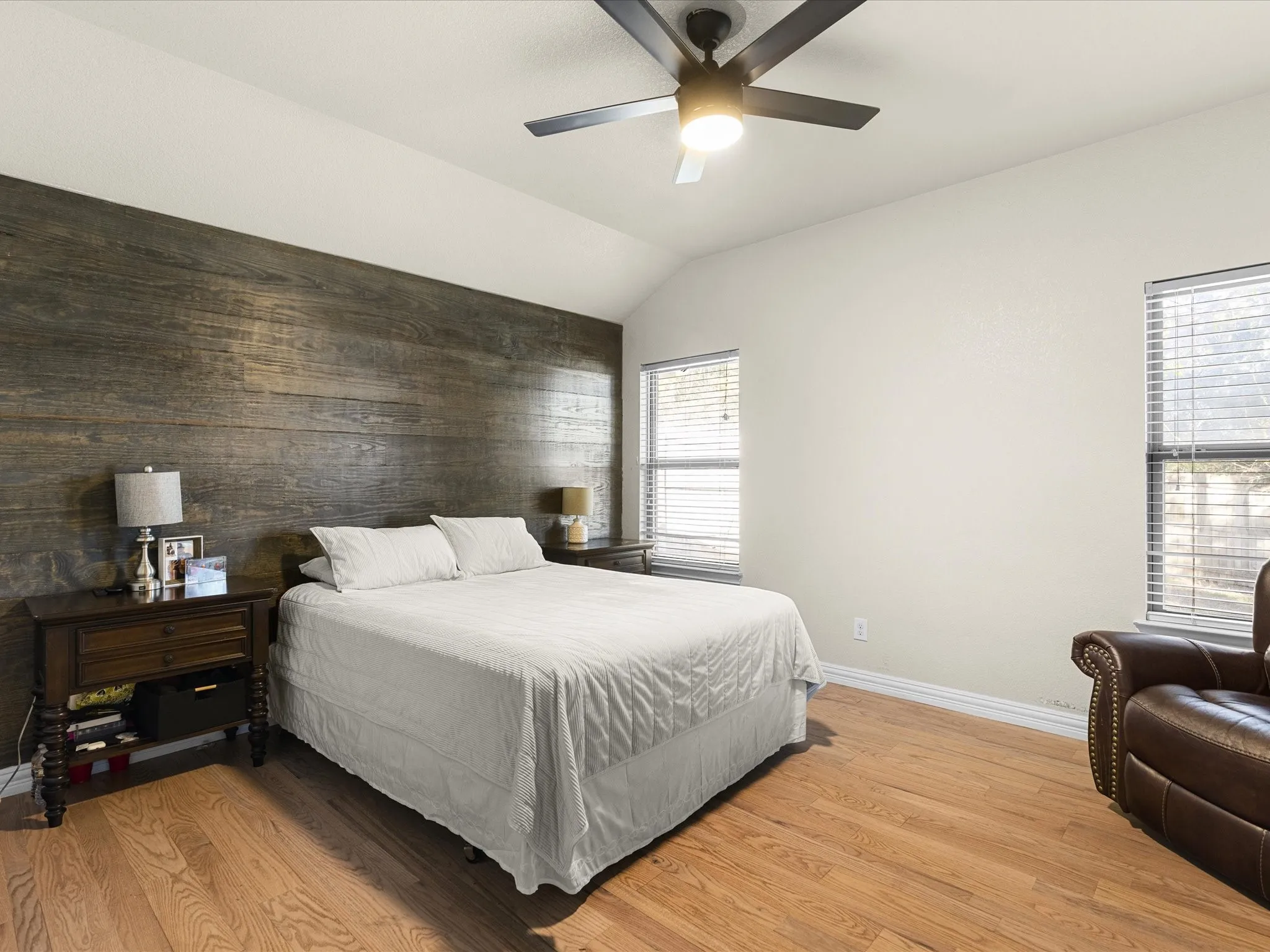 Bedroom featuring light wood-style flooring, ceiling fan, vaulted ceiling, wooden walls, and an accent wall
