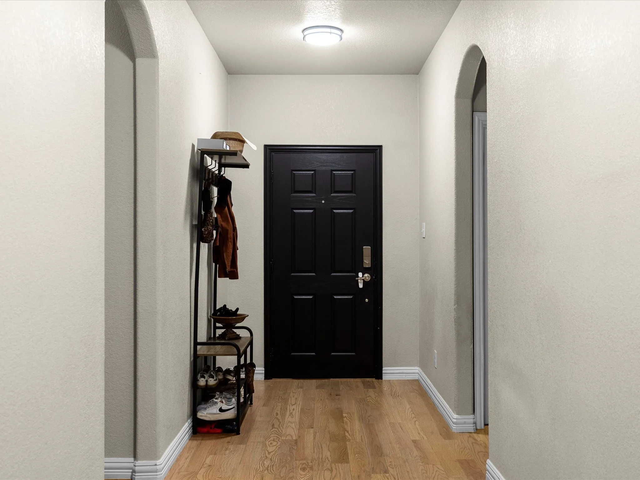 Foyer entrance featuring arched walkways, a textured wall, and light wood-style flooring