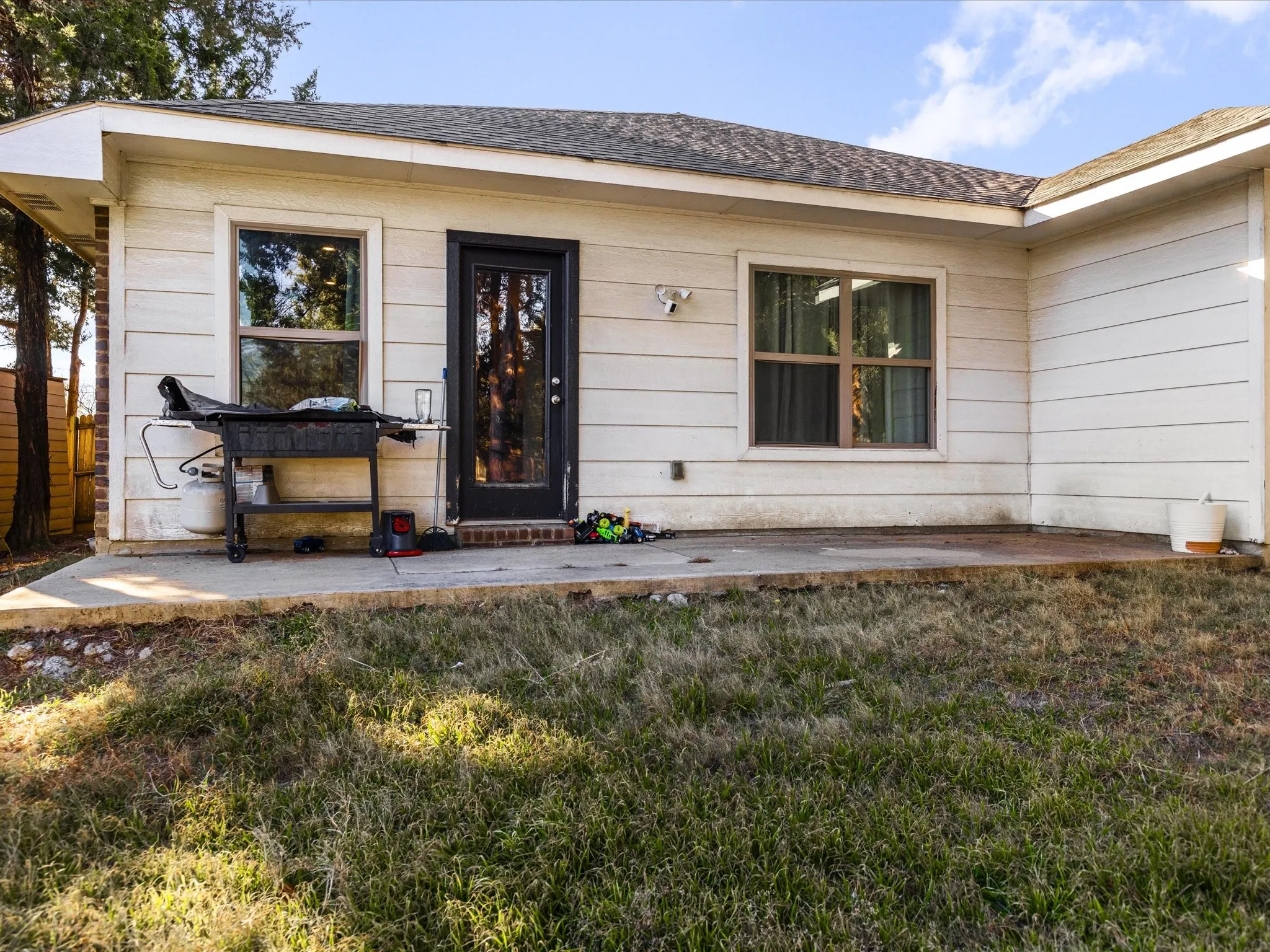 Entrance to property with a patio area, a lawn, and roof with shingles