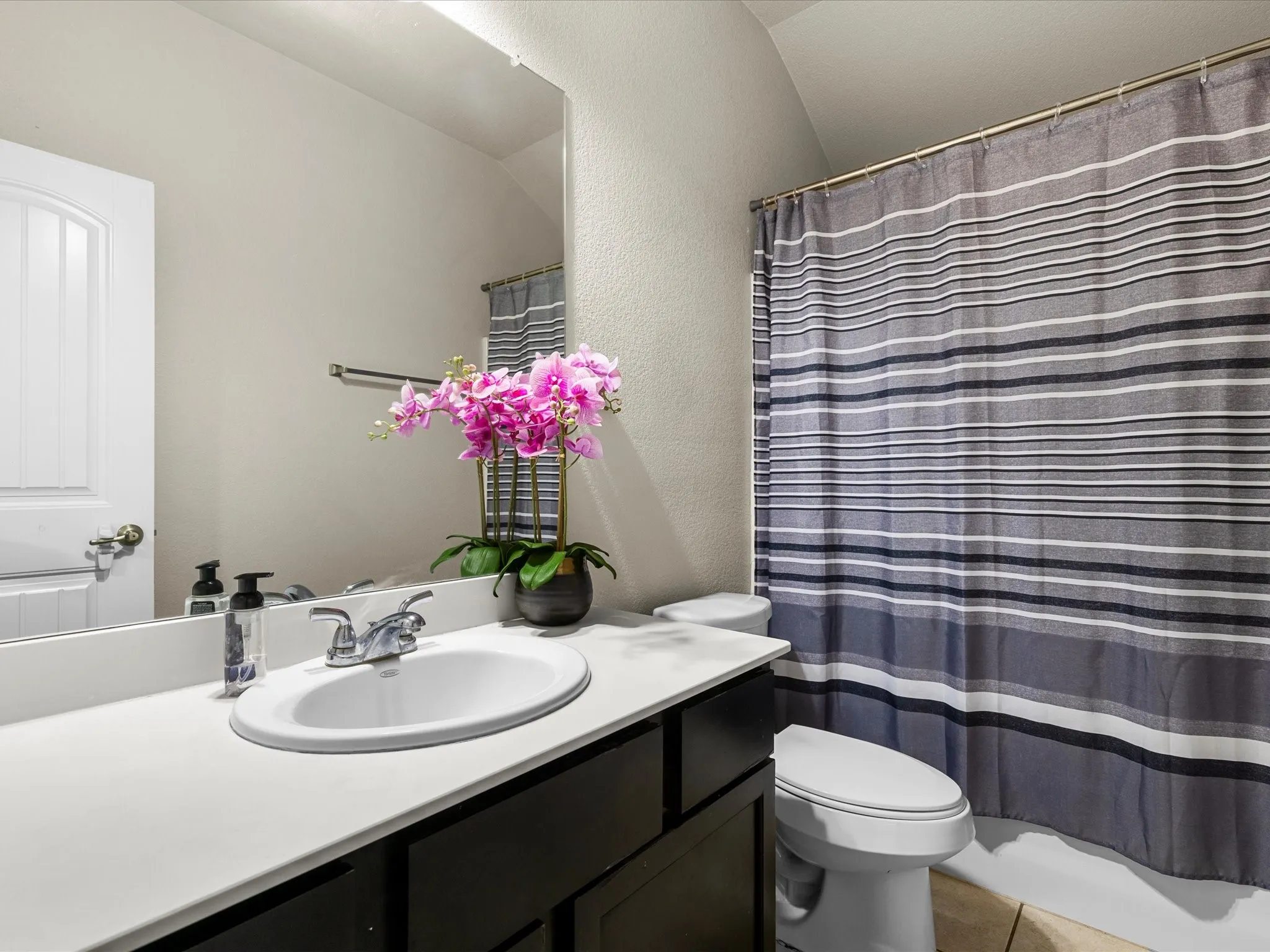 Full bath with vanity, lofted ceiling, a textured wall, and tile patterned flooring