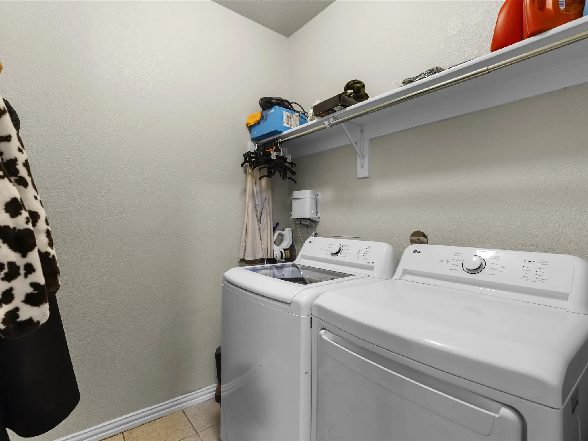 Laundry room featuring a textured wall, washing machine and clothes dryer, and light tile patterned floors