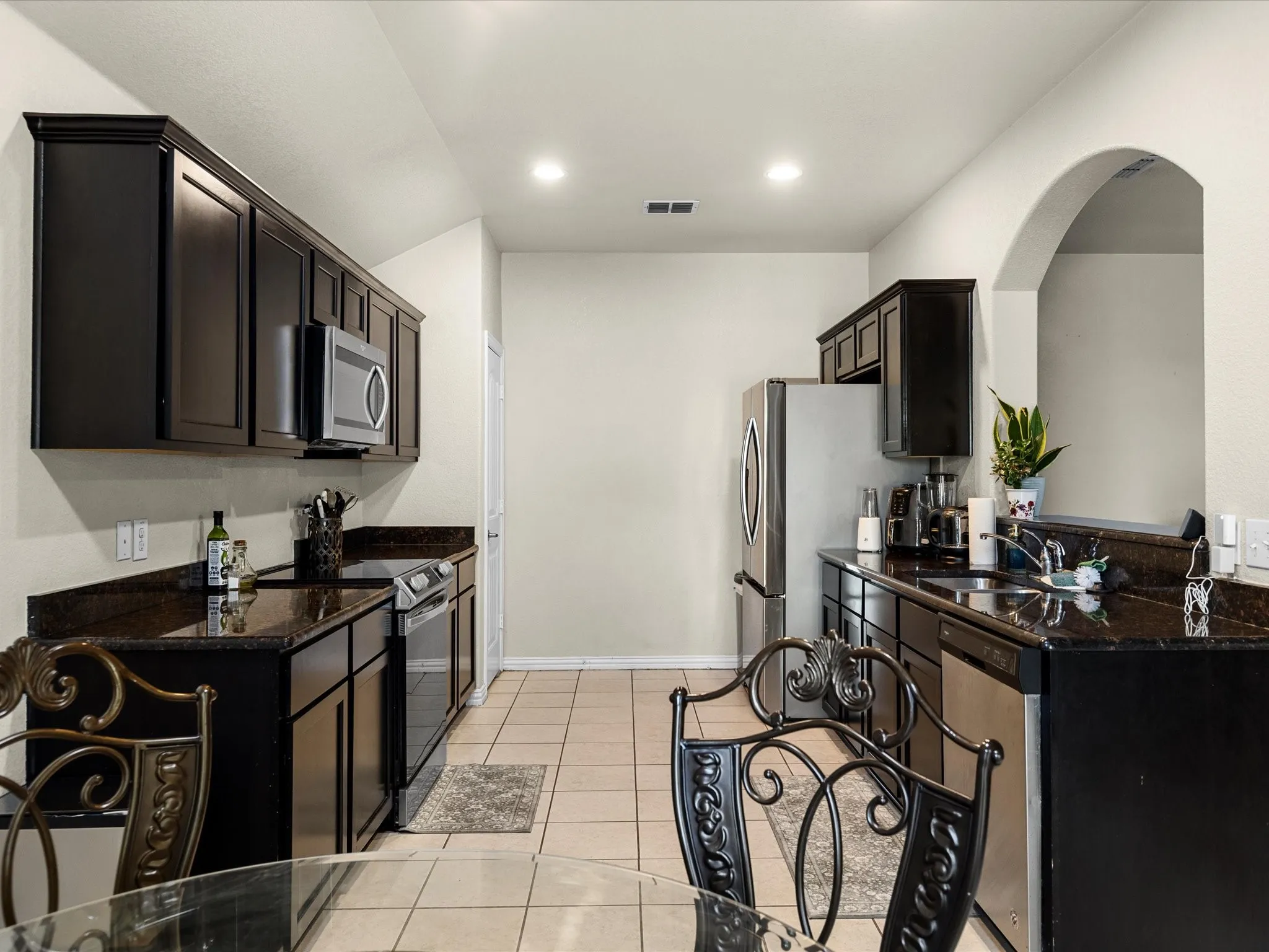 Kitchen with dark stone counters, stainless steel appliances, light tile patterned floors, and recessed lighting
