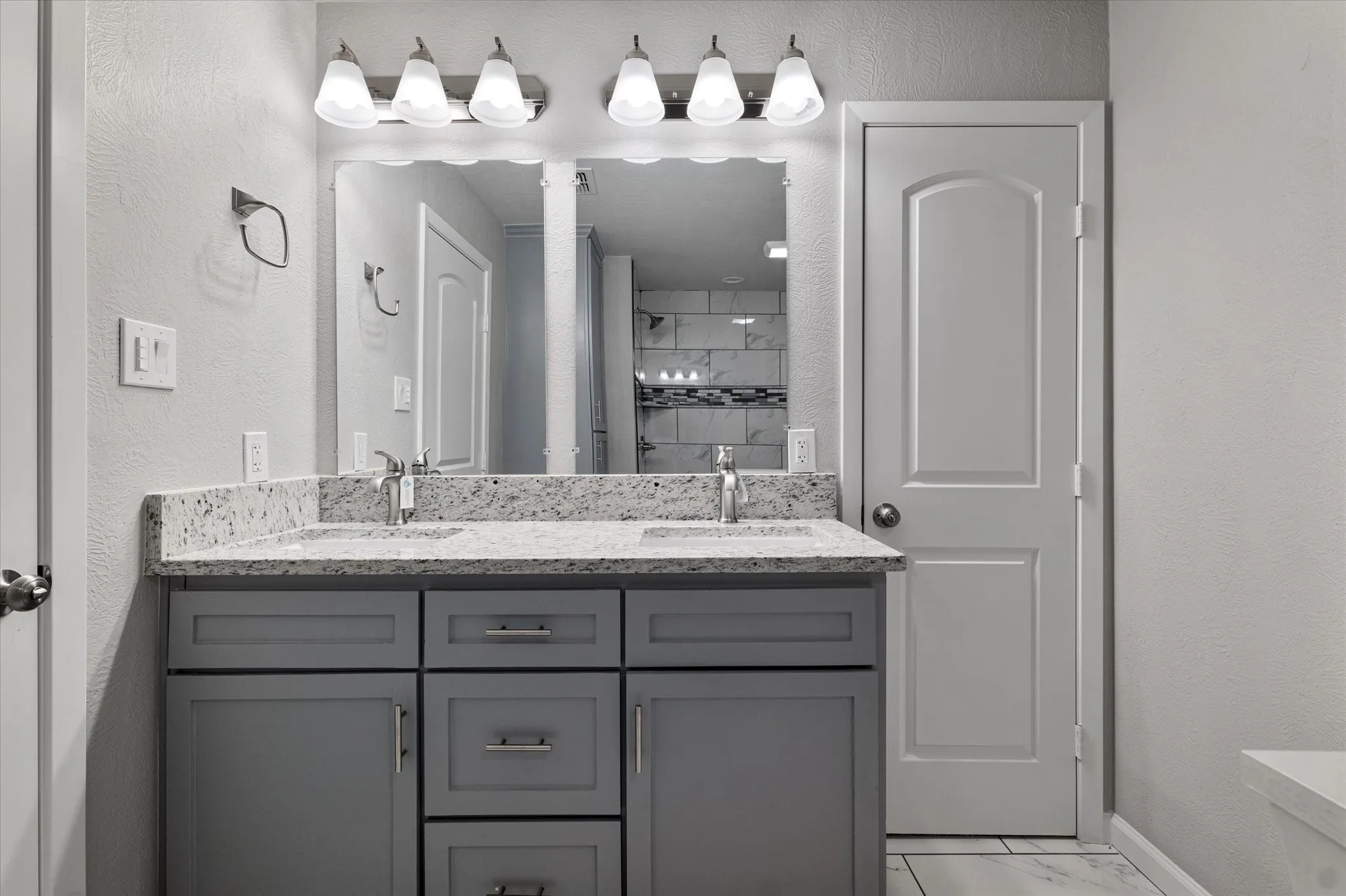 Bathroom featuring a textured wall, double vanity, tiled shower, and light marble finish flooring