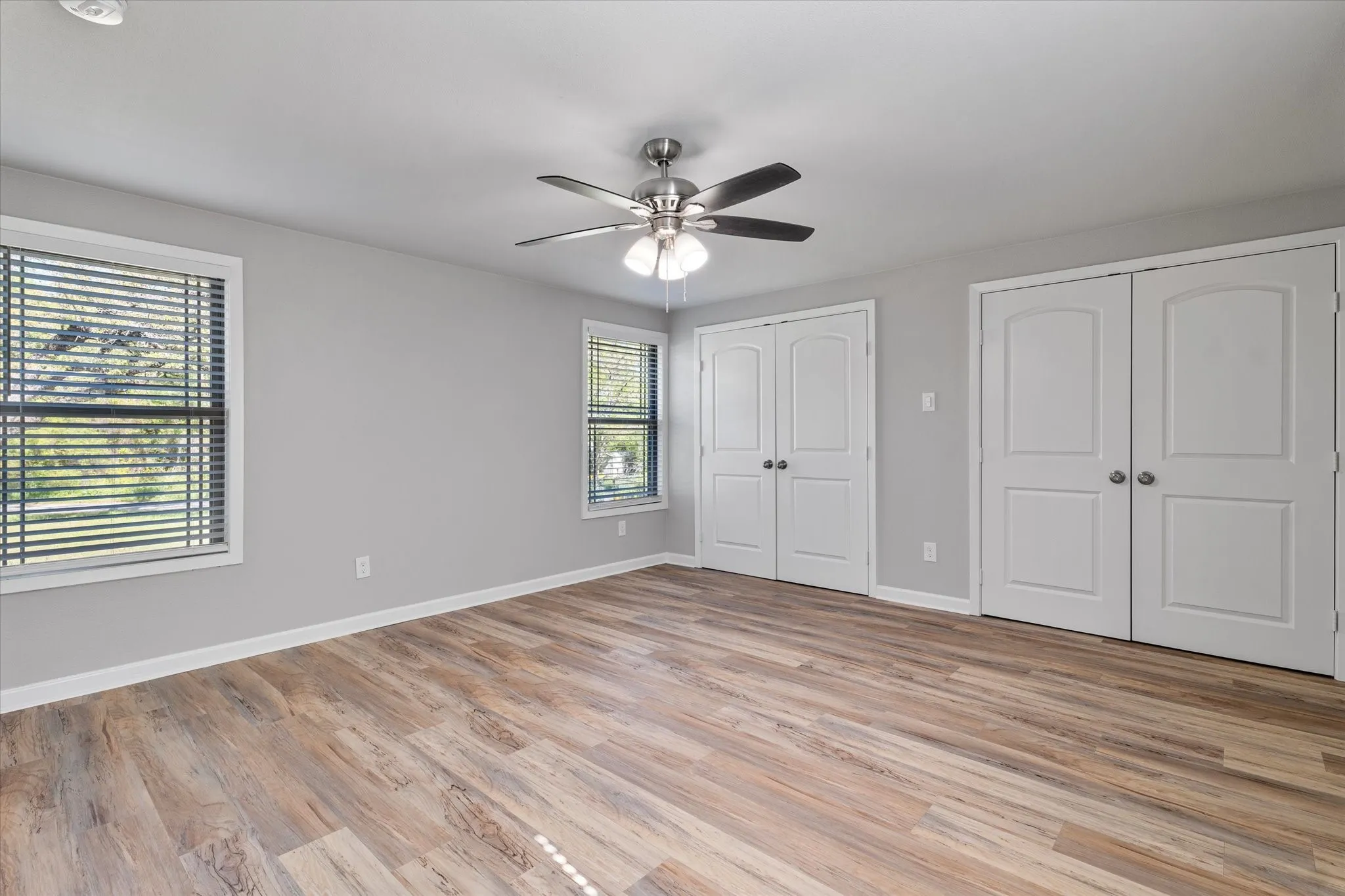 Unfurnished bedroom featuring two closets, light wood-style floors, and a ceiling fan