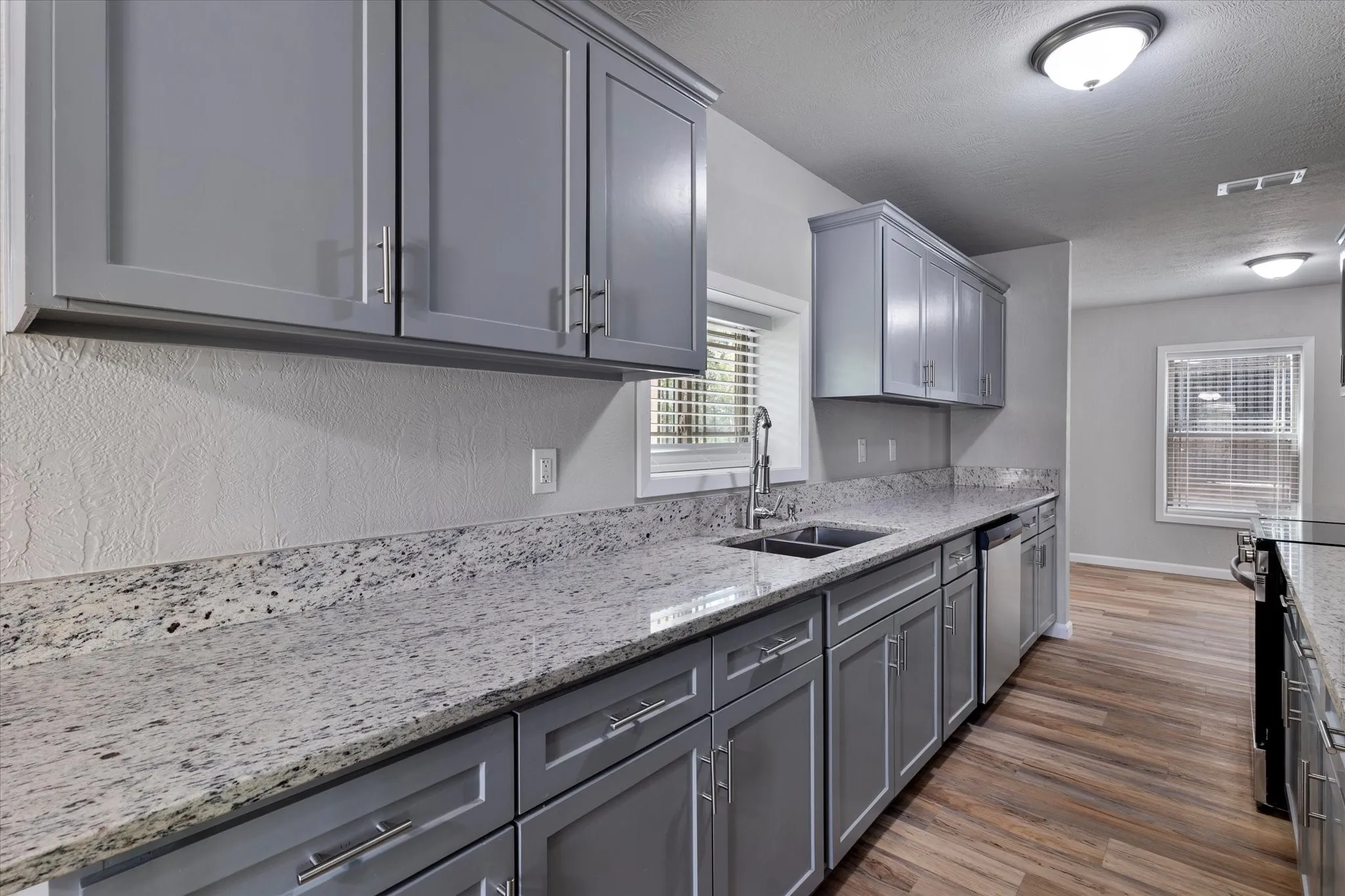 Kitchen with gray cabinets, light stone counters, dark wood-style floors, range with electric cooktop, and a textured ceiling