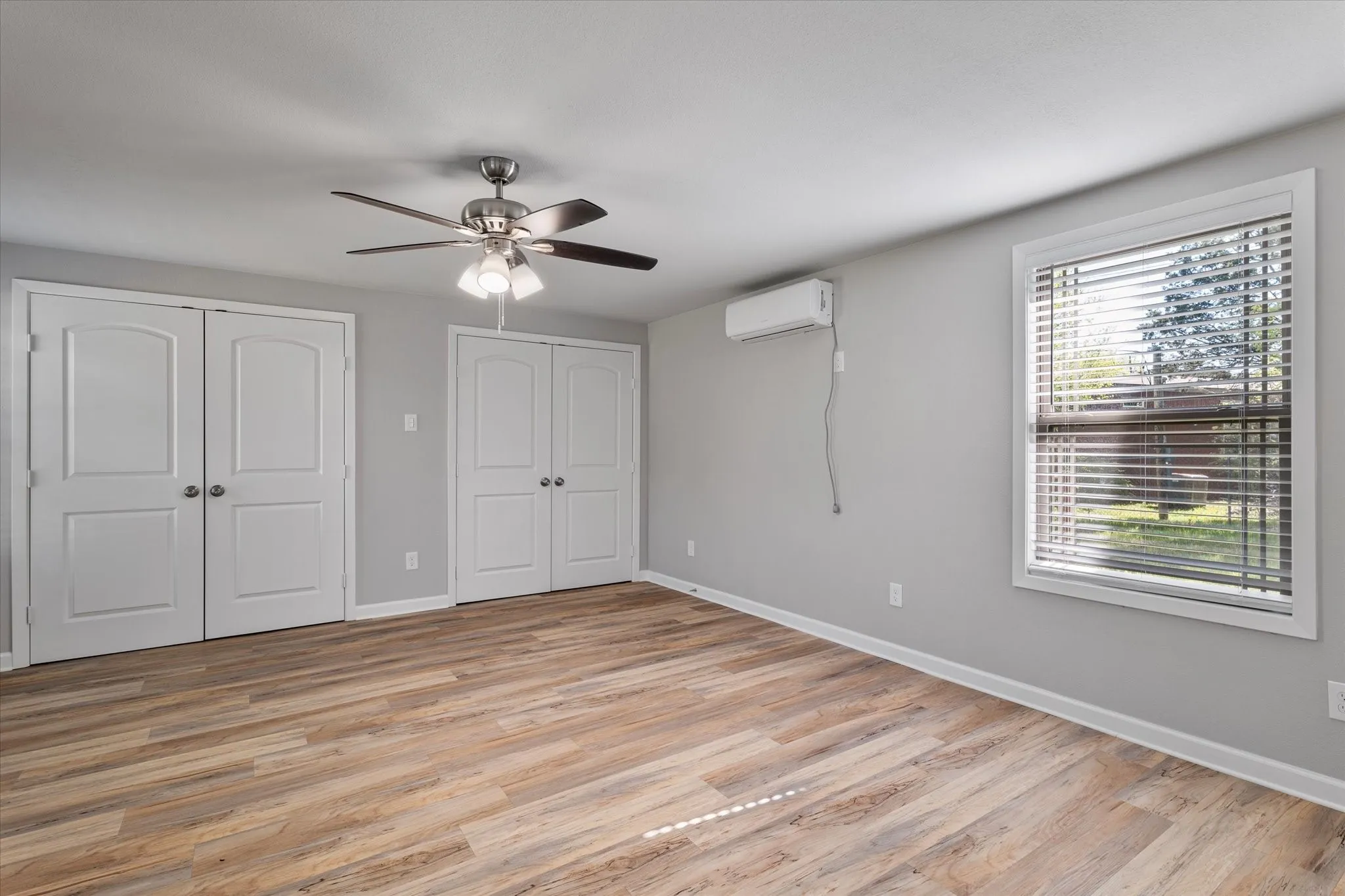 Unfurnished bedroom with two closets, light wood-type flooring, and a ceiling fan