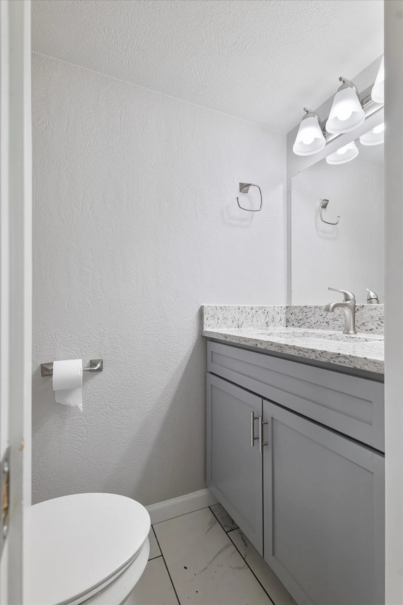 Half bathroom featuring vanity, light marble finish flooring, and a textured ceiling