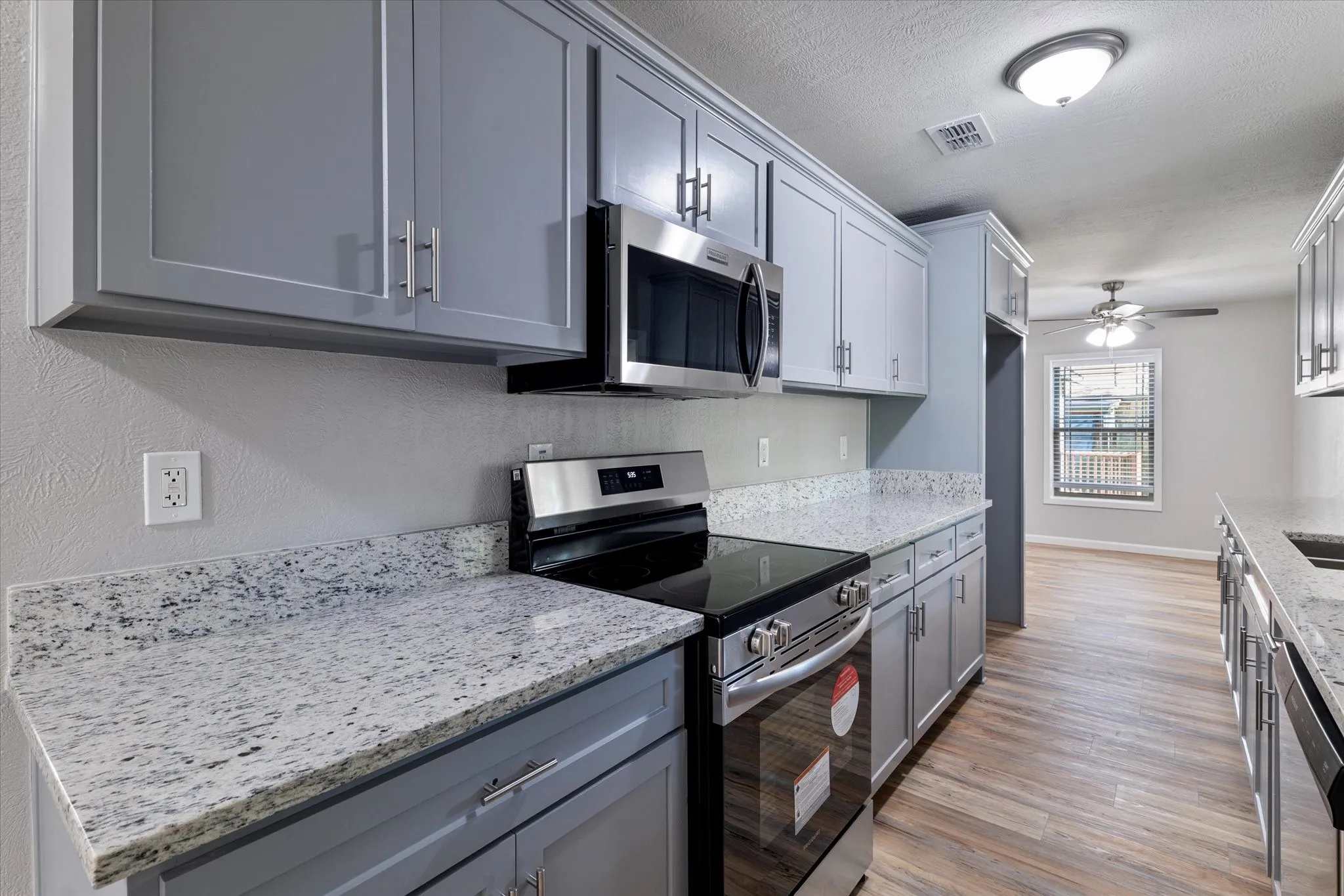 Kitchen featuring stainless steel appliances, light stone countertops, gray cabinets, ceiling fan, and a textured ceiling