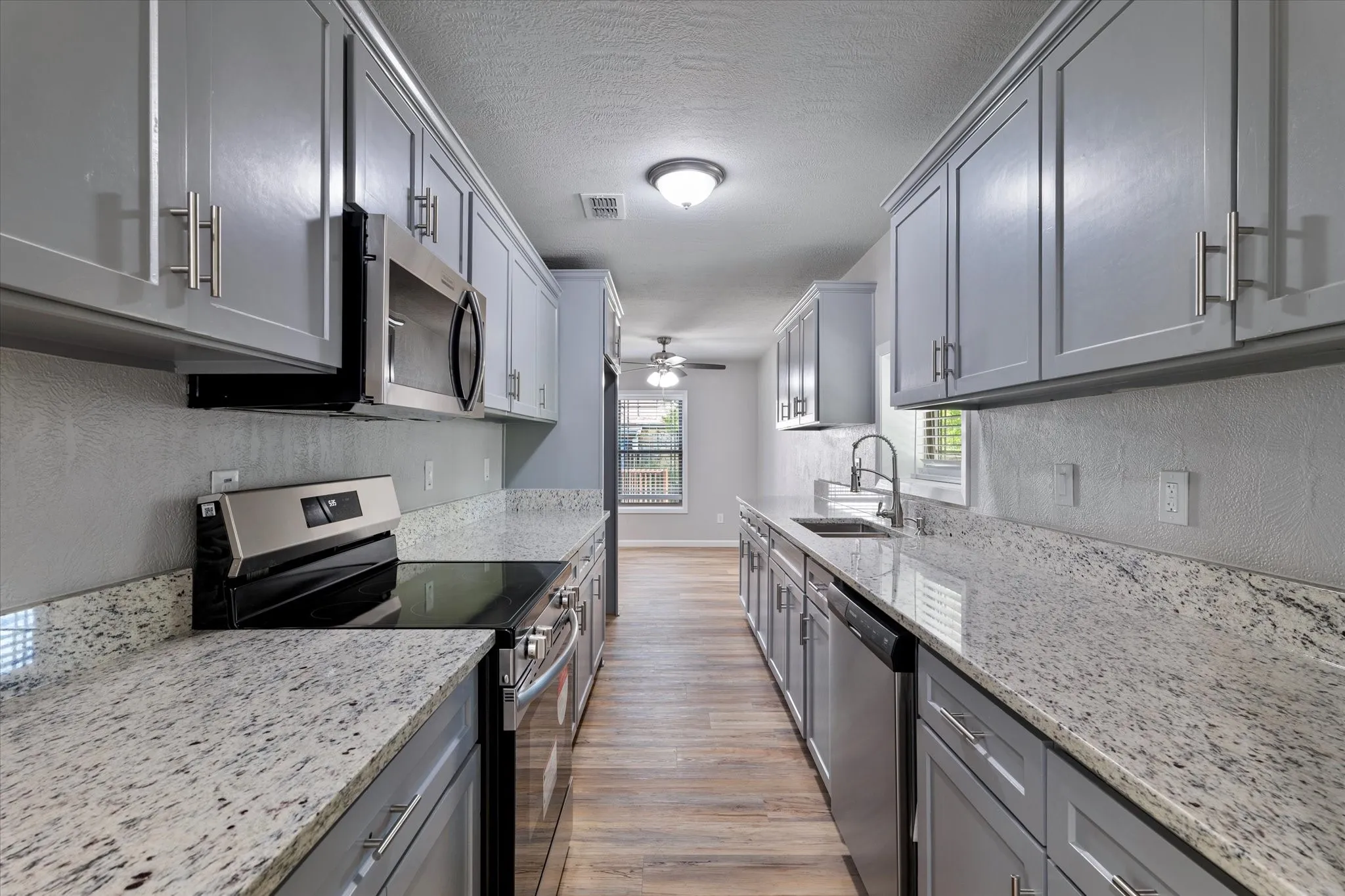Kitchen featuring stainless steel appliances, gray cabinets, light wood-type flooring, light stone countertops, and ceiling fan