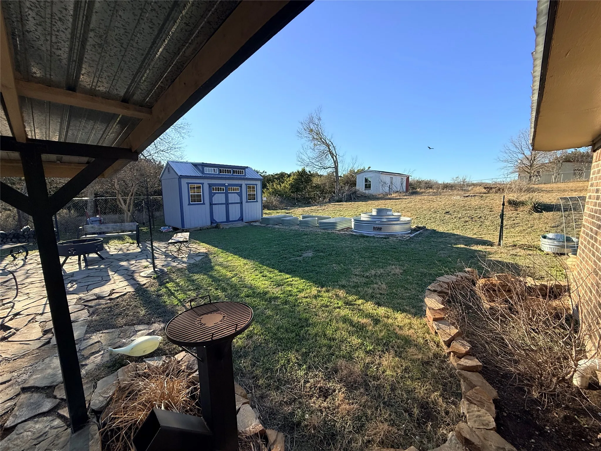 View of grassy yard featuring a patio area, an outdoor fire pit, and a storage unit