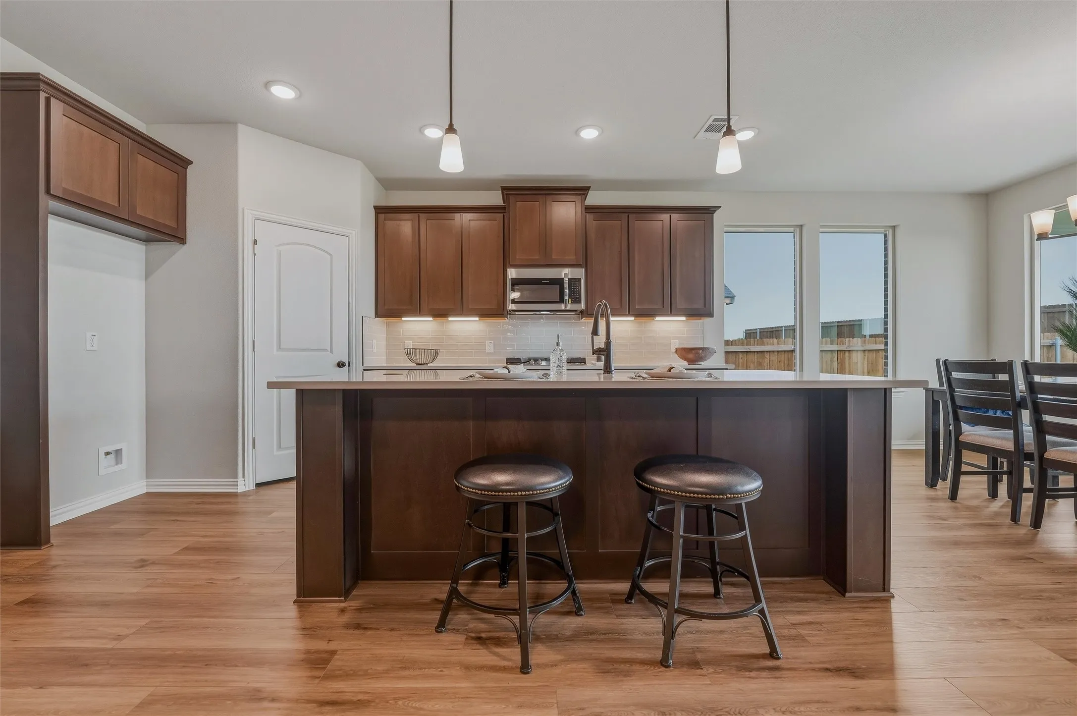 Open-concept kitchen featuring wood-finish flooring, dark wood cabinetry, a central island with countertop seating, stainless steel appliances, and pendant lighting
