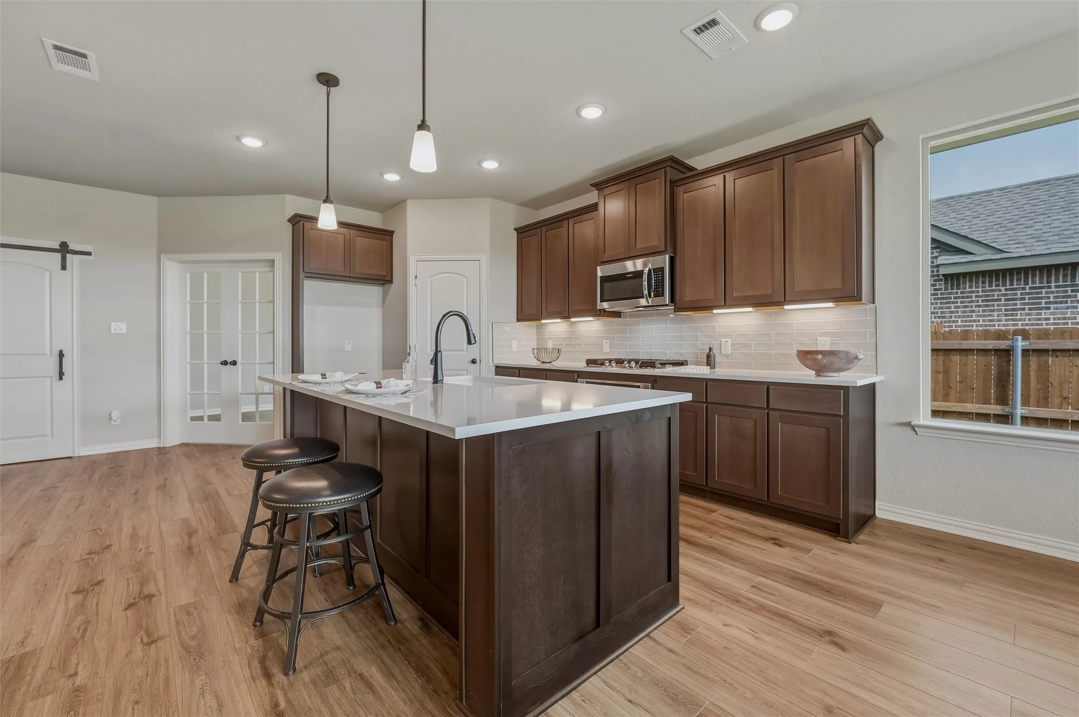 Kitchen featuring a central island, wood-finish flooring, dark wood cabinetry, white countertops, and a subway tile backsplash