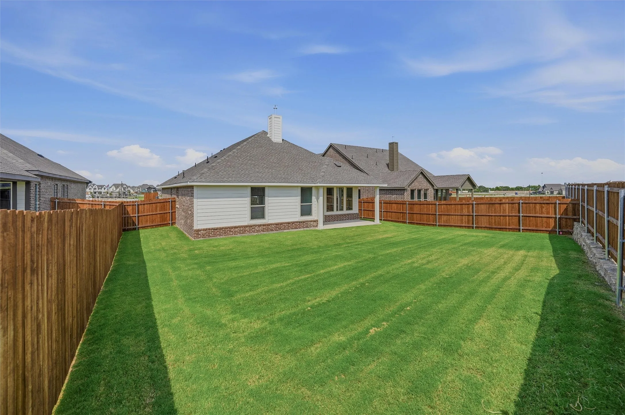Expansive lawn with a full privacy fence, covered patio, and brick and siding exterior