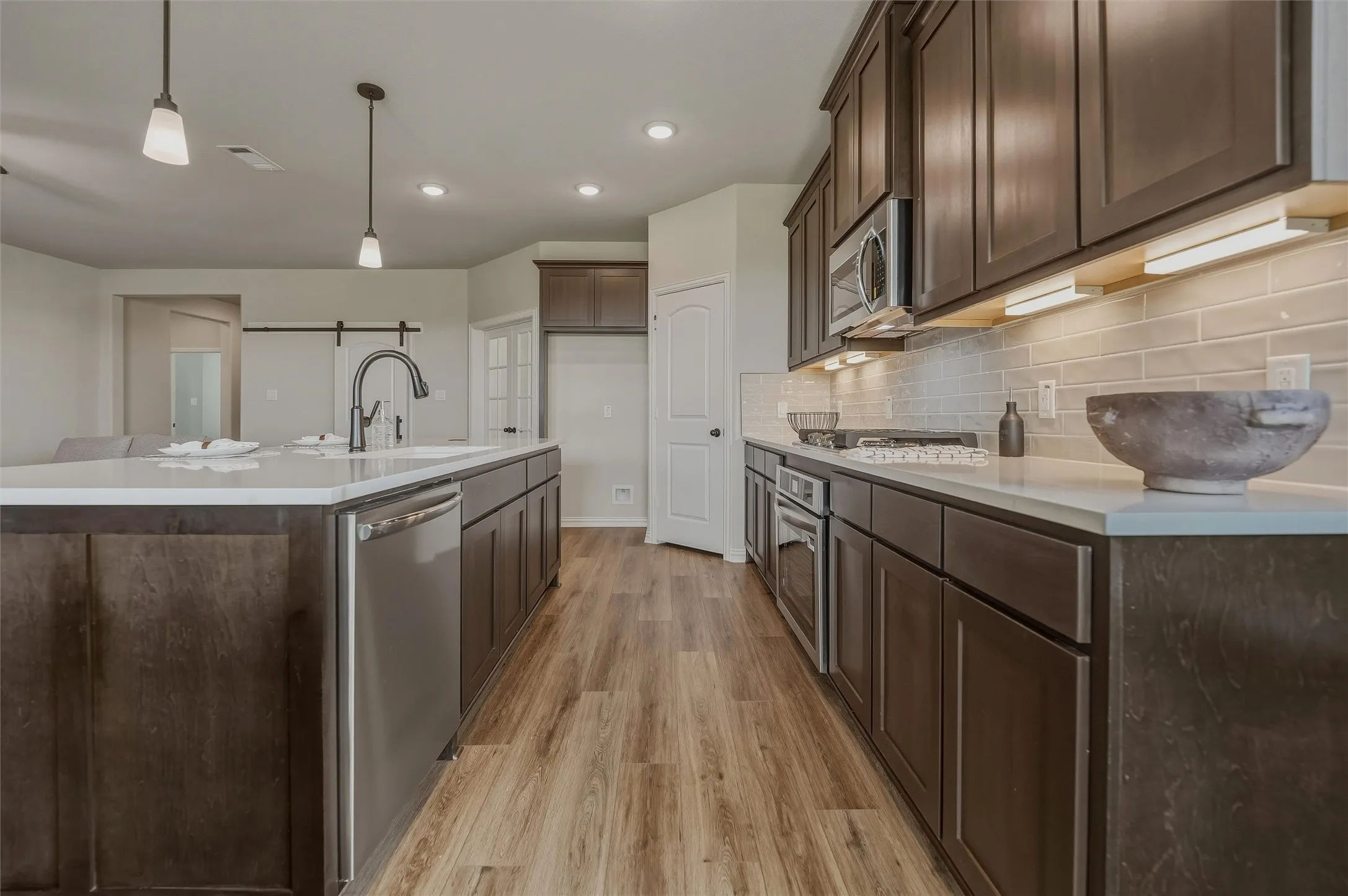 Expansive kitchen featuring wood-finish flooring, dark wood-finish cabinetry, light countertops, a built-in stainless steel dishwasher, and stainless steel appliances