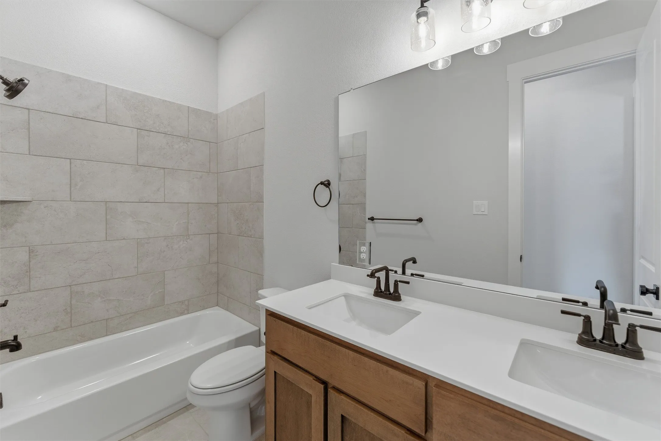 Bathroom featuring a dual vanity with a light wood-finish cabinet and white countertops, a large mirror, and a tub-shower combination with light-toned rectangular wall tile
