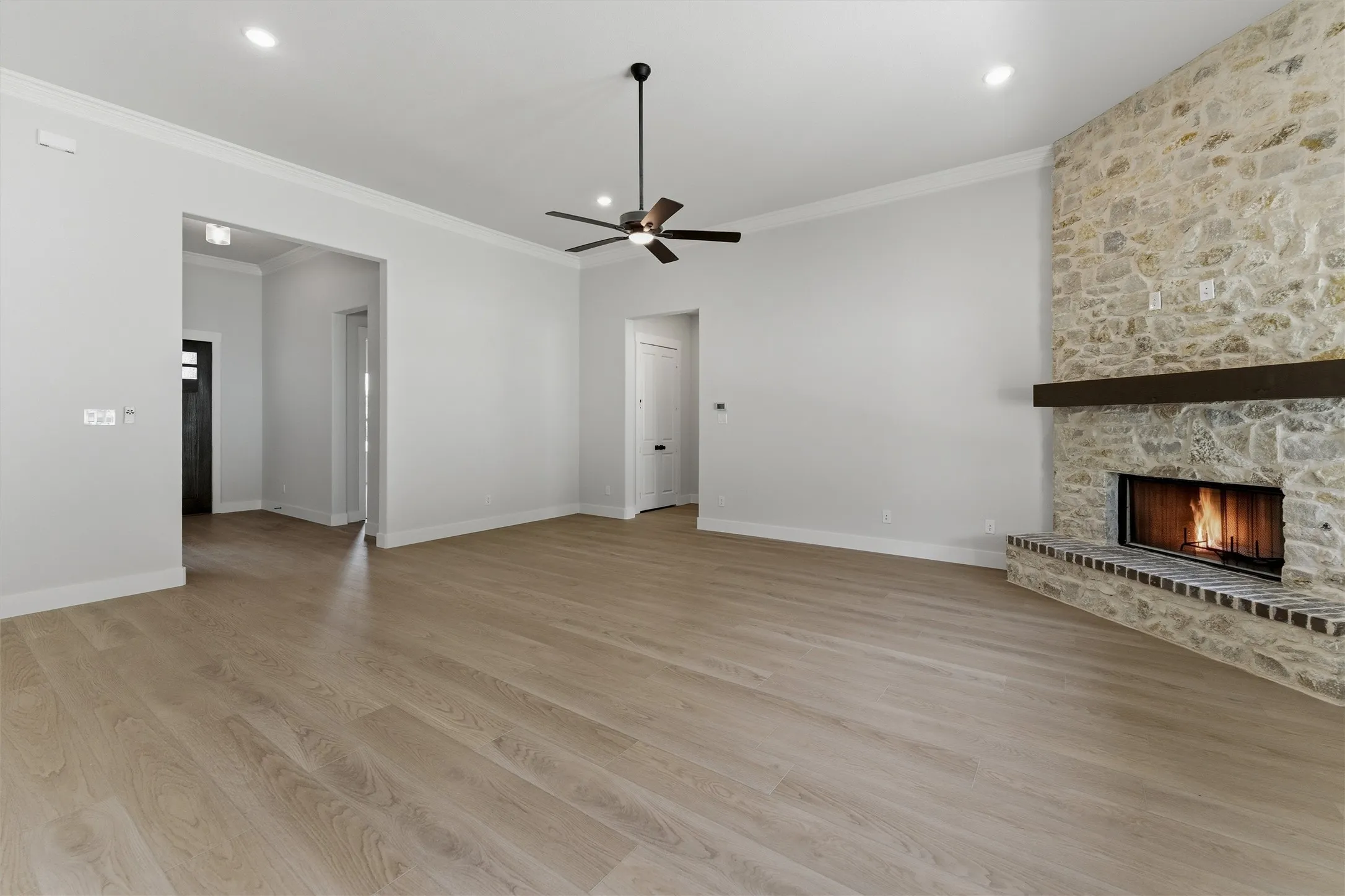 Spacious living area featuring a floor-to-ceiling stone fireplace with a dark wood mantel, light wood-finish flooring, recessed lighting, and a ceiling fan