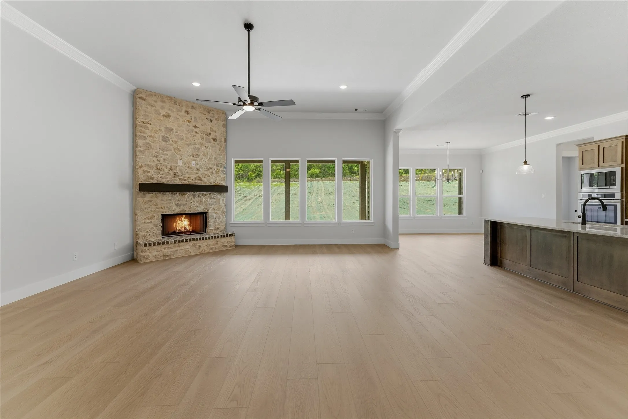 Spacious living area featuring light wood-finish flooring, a stone-clad fireplace with a dark wood mantel, and a ceiling fan