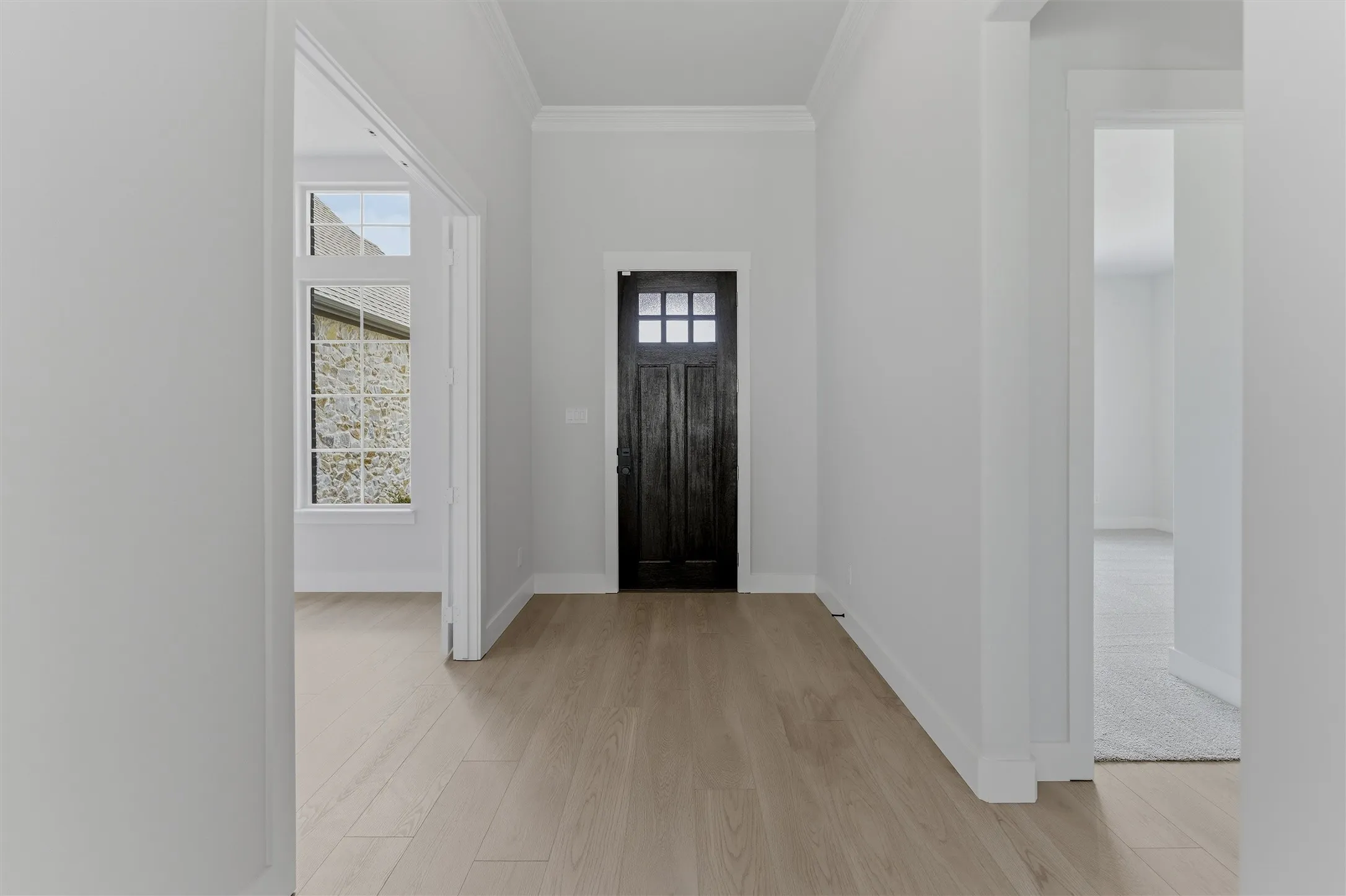 Entryway featuring light wood-finish flooring, a dark paneled door with glass inserts, and crown molding