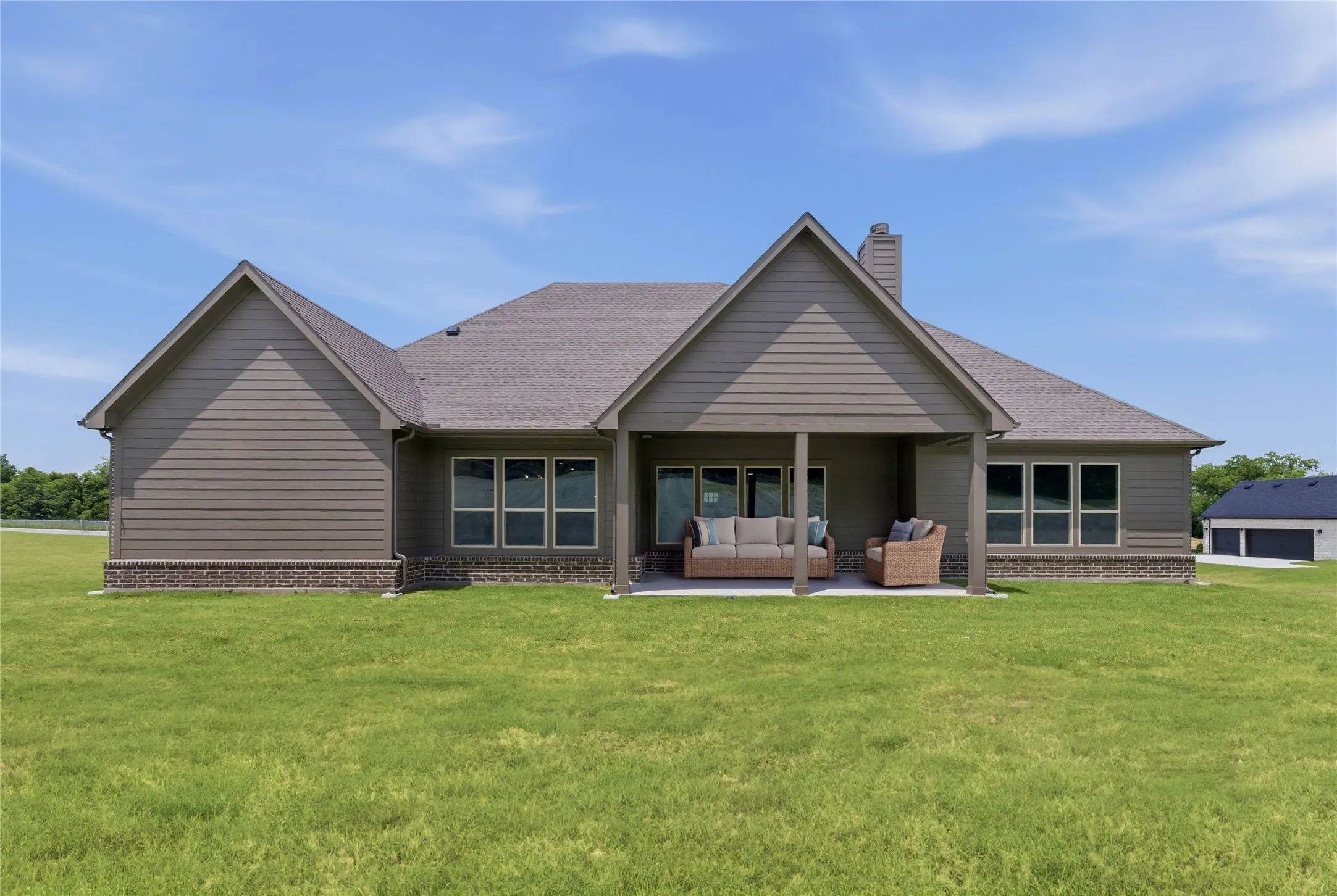 Rear exterior featuring an expansive lawn, covered patio, multiple windows, and a detached structure