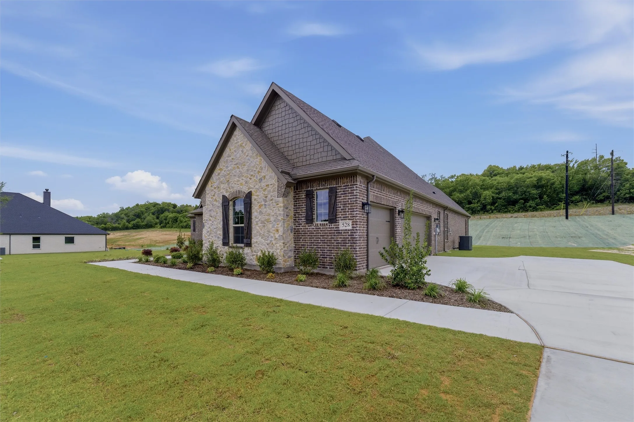 Stone and brick exterior with a multi-car garage, mature landscaping, and a concrete driveway